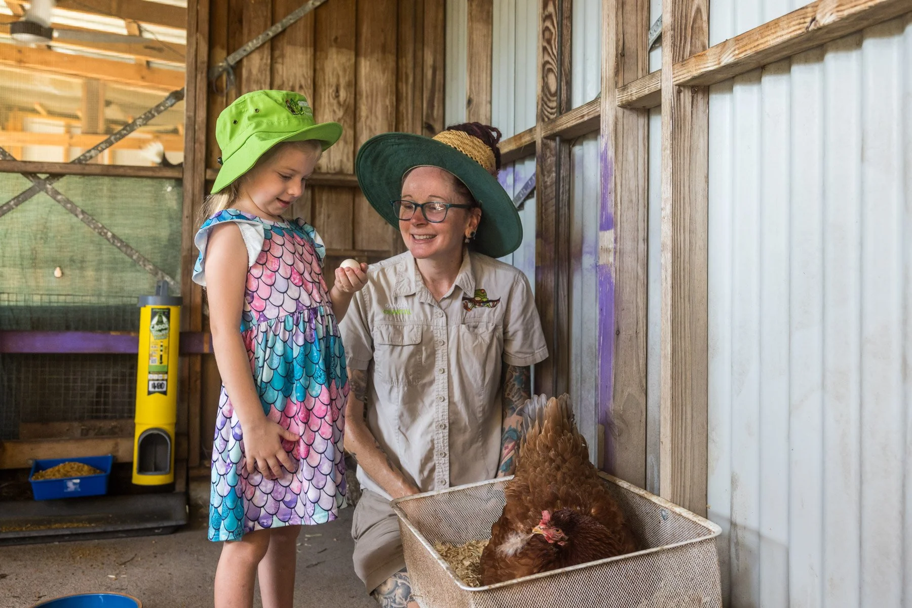 A woman and a girl interacting with chickens in a barn, with the woman showing the girl an egg.