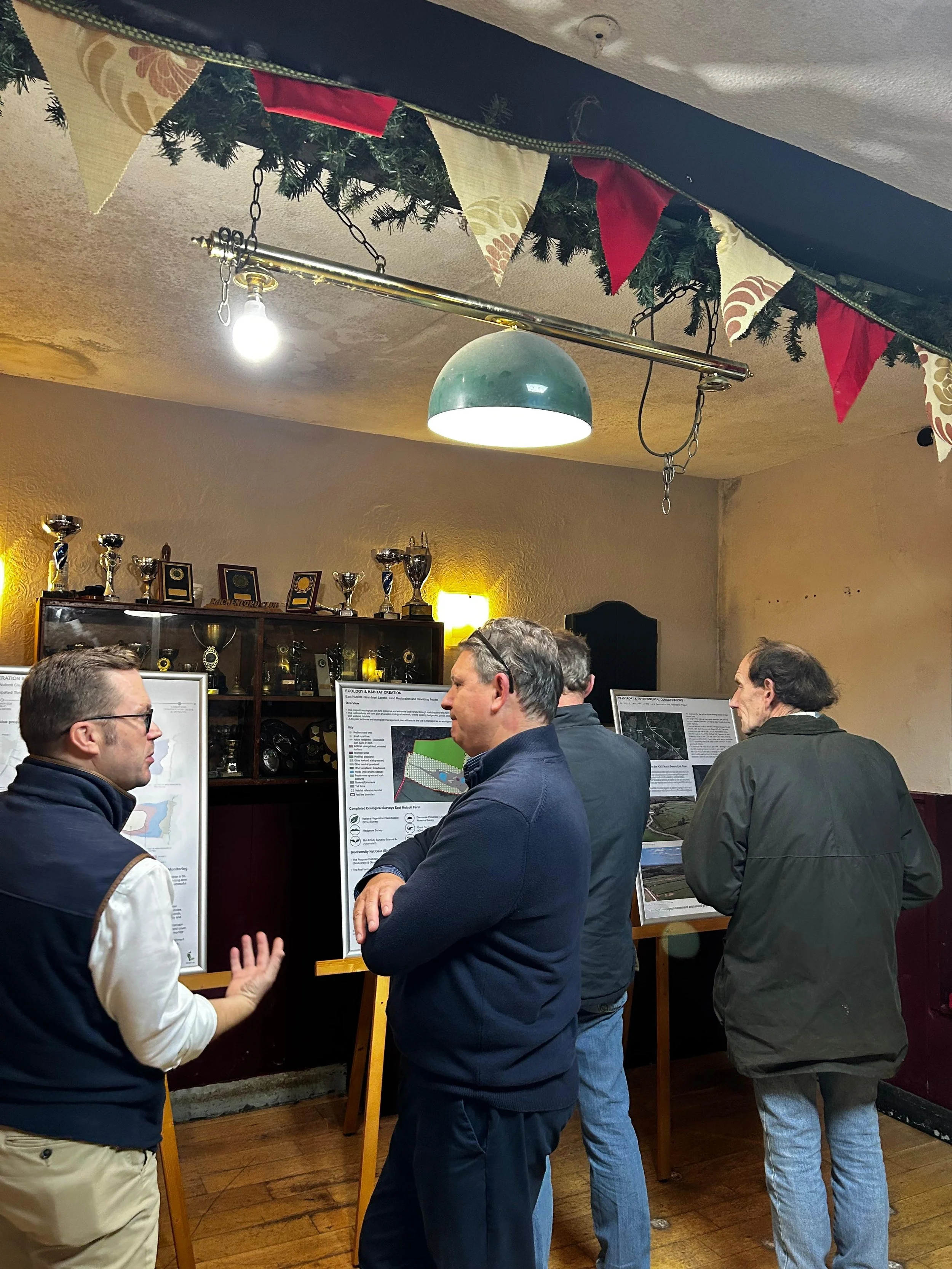 People discussing at an indoor presentation or poster display in a room decorated with holiday banners and trophies on a shelf.