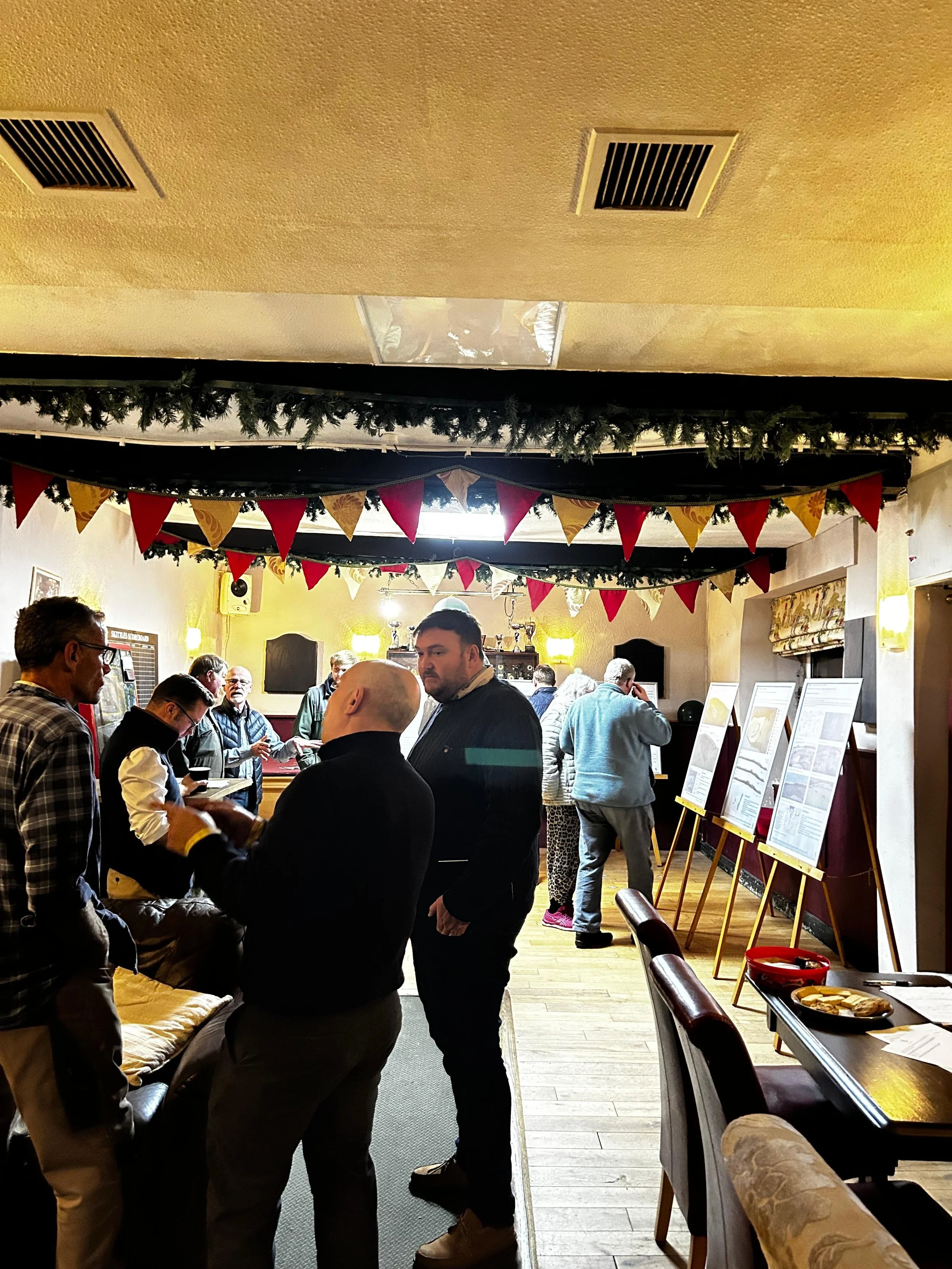 People gathered inside a cozy, decorated restaurant with Christmas banners and greenery on the ceiling, reading menus on easels.