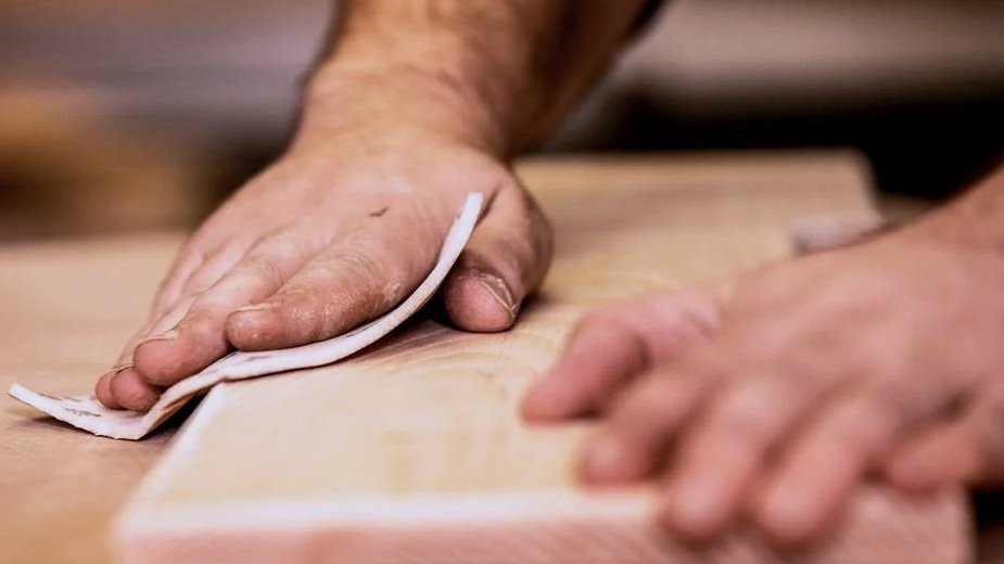 A person sanding a wooden surface with a hand sanding cloth or pad.