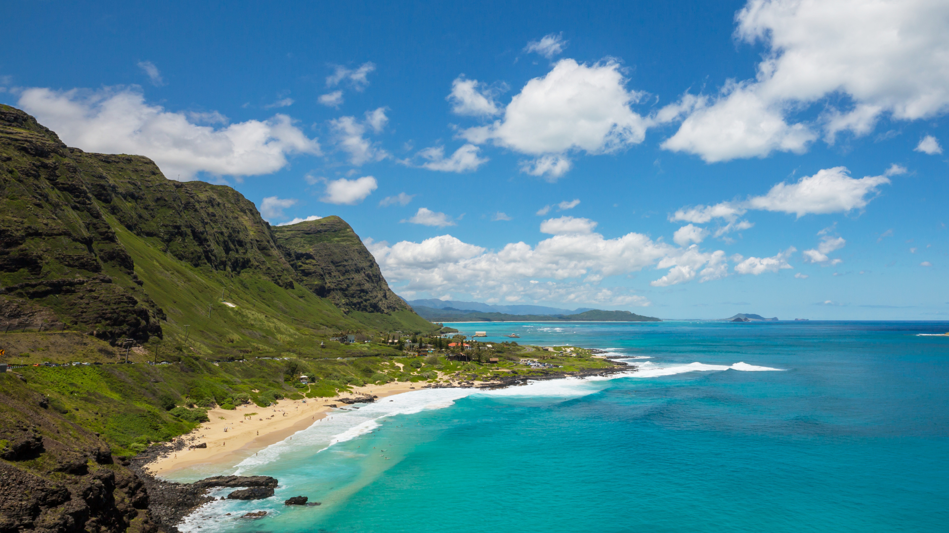 A Hawaii beach scene with rugged green hills and the Pacific ocean