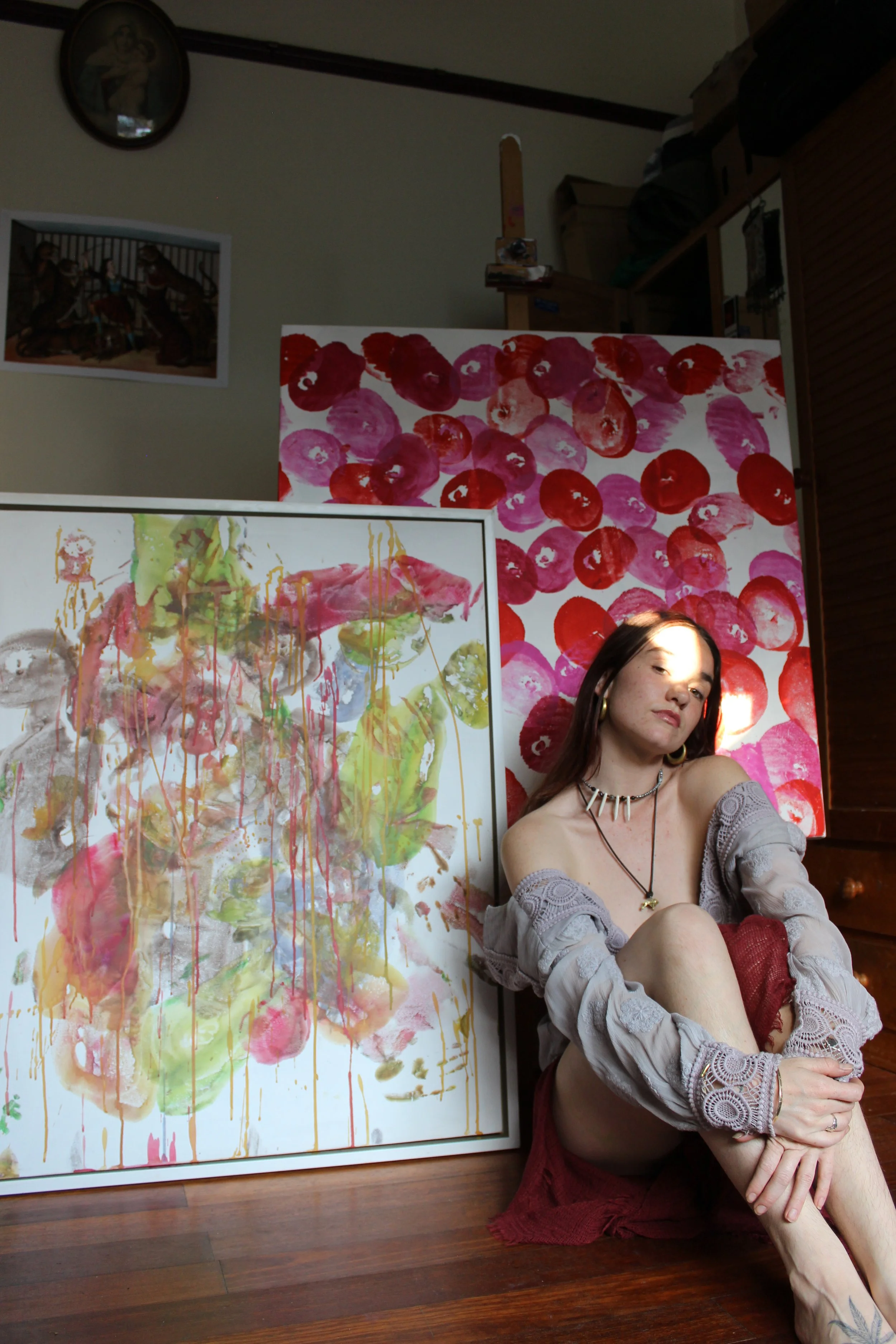 Woman sitting on the floor next to colorful abstract paintings in a room.