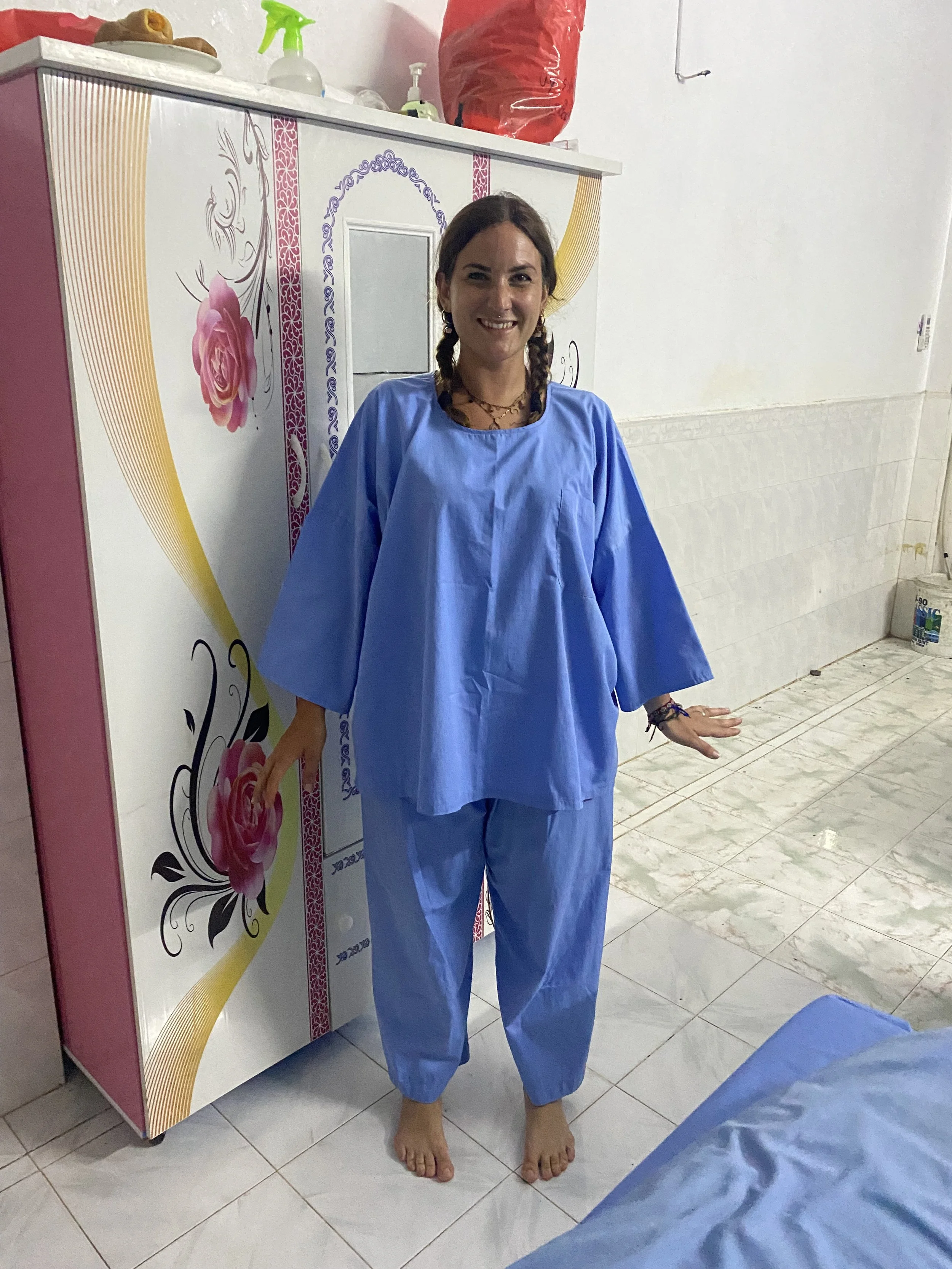 Una donna sorridente indossa una divisa azzurra in un ambiente domestico, con fondo di armadio decorato con rose e pareti bianche