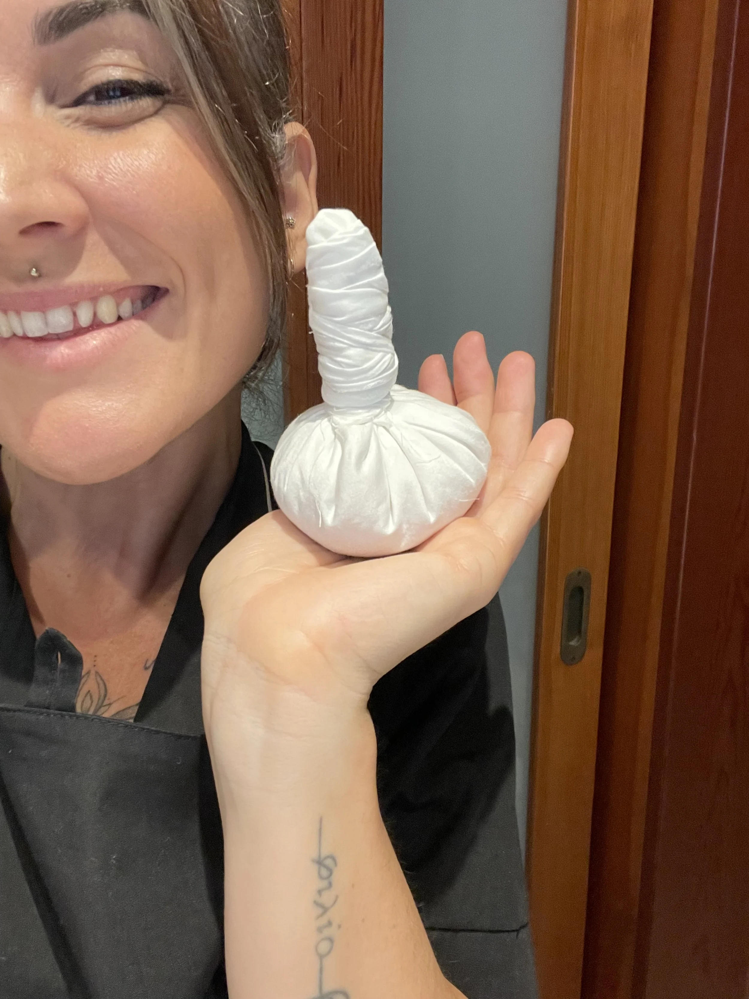 Una donna con un sorriso, tiene in mano un fagotto di erbe utilizzato per fare i massaggi.