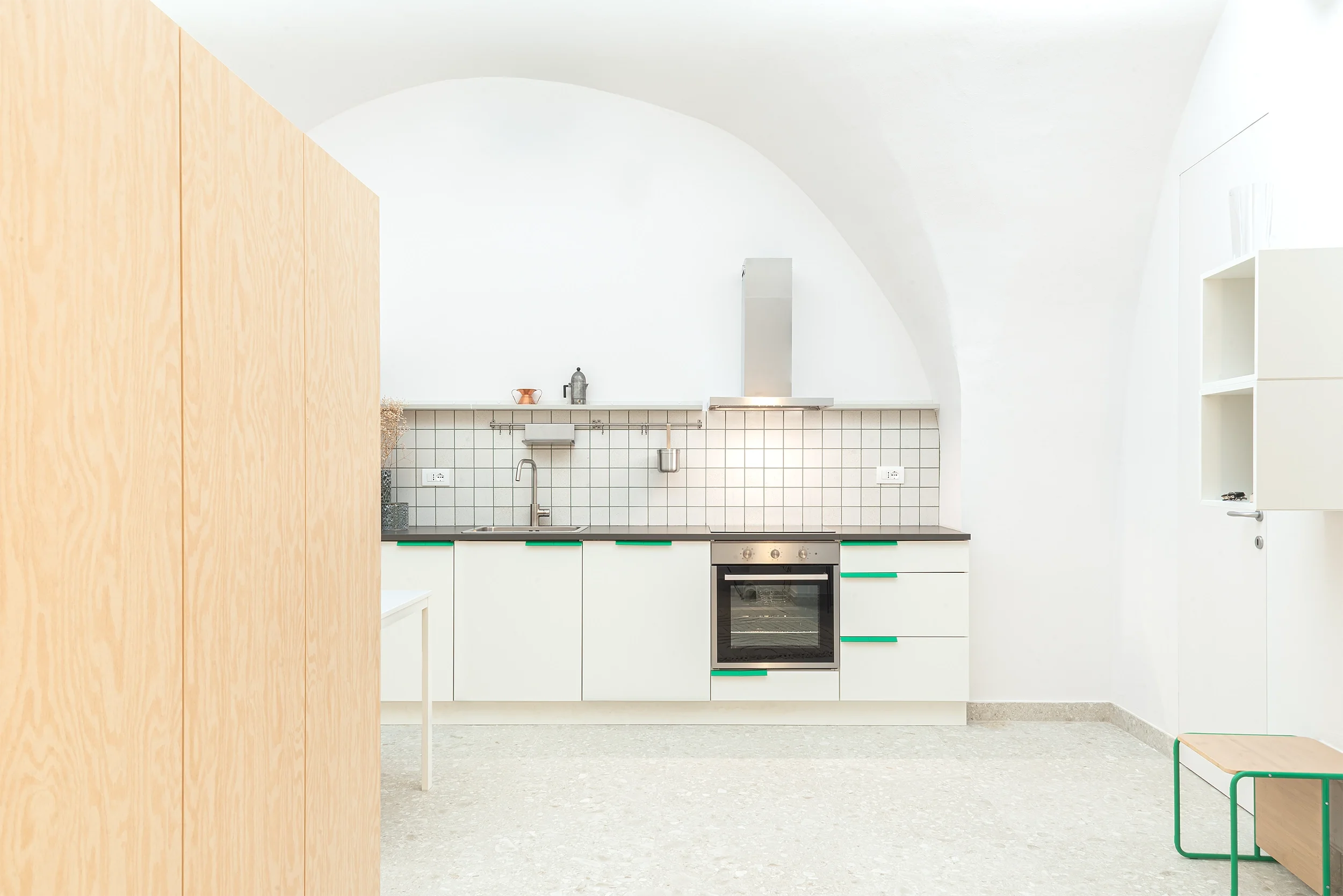 Cucina minimalista con bianco, legno chiaro e dettagli verdi, e una parete a volta with piano di lavoro e forno.