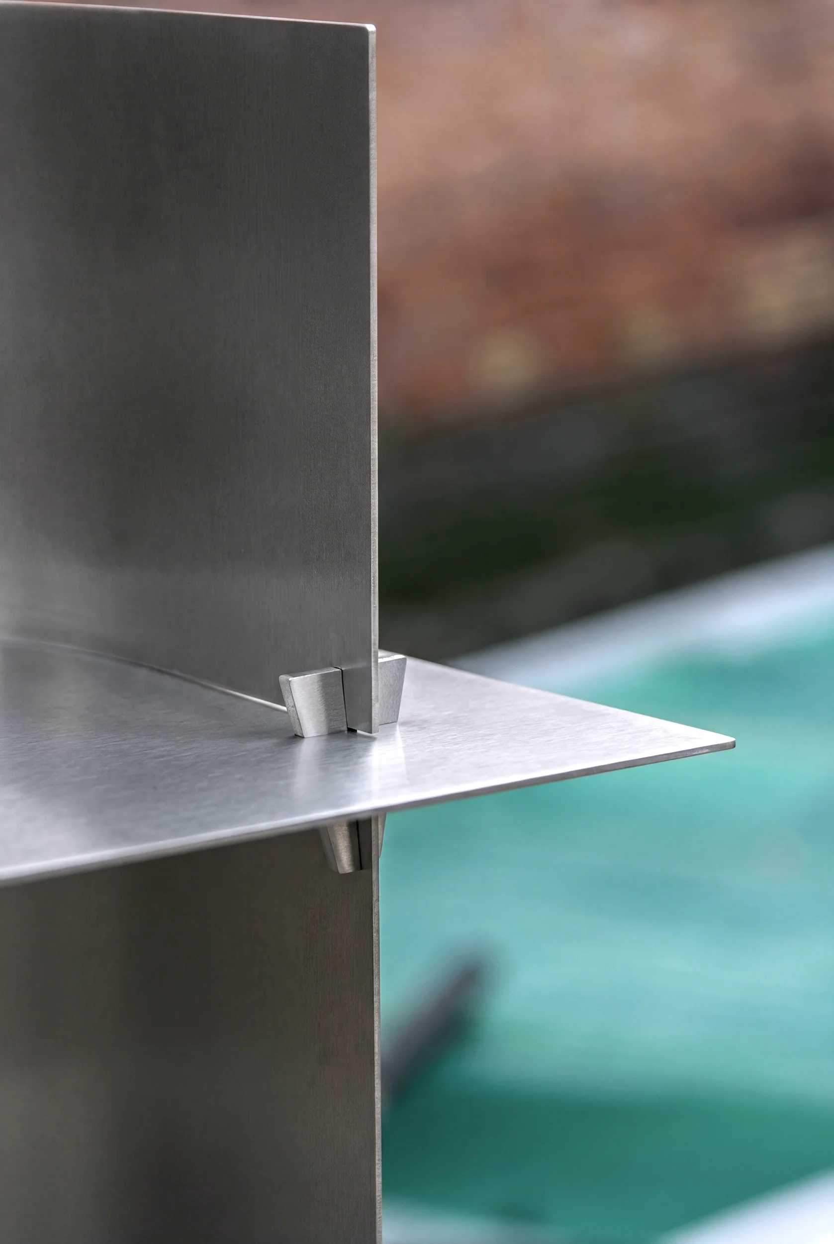 Dettaglio di una struttura in metallo con una parete e una superficie orizzontale, con uno sfondo sfocato che sembra un ambiente interno o esterno.