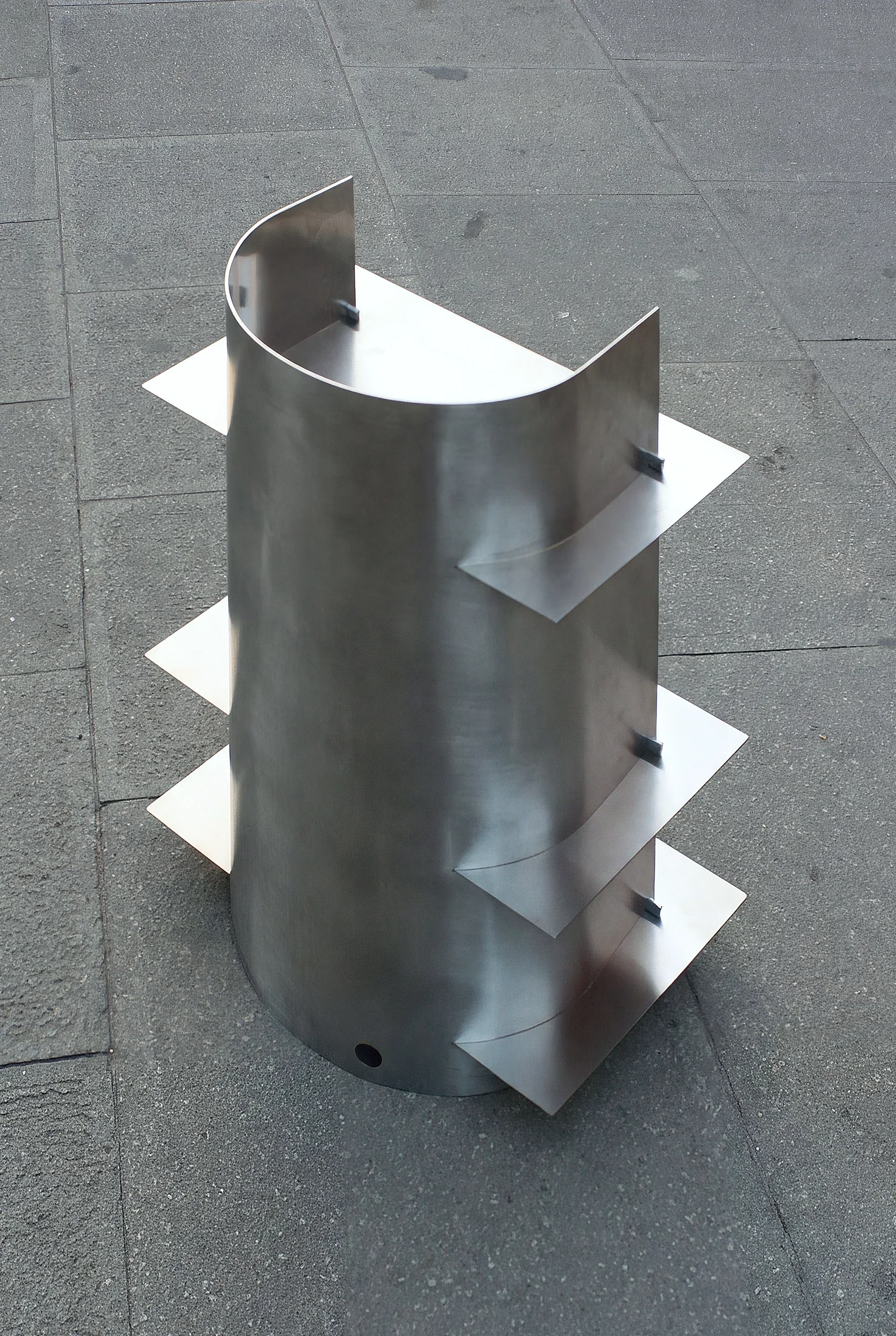 Struttura di metallo curvata con piani orizzontali, situata su una superficie in pietra.