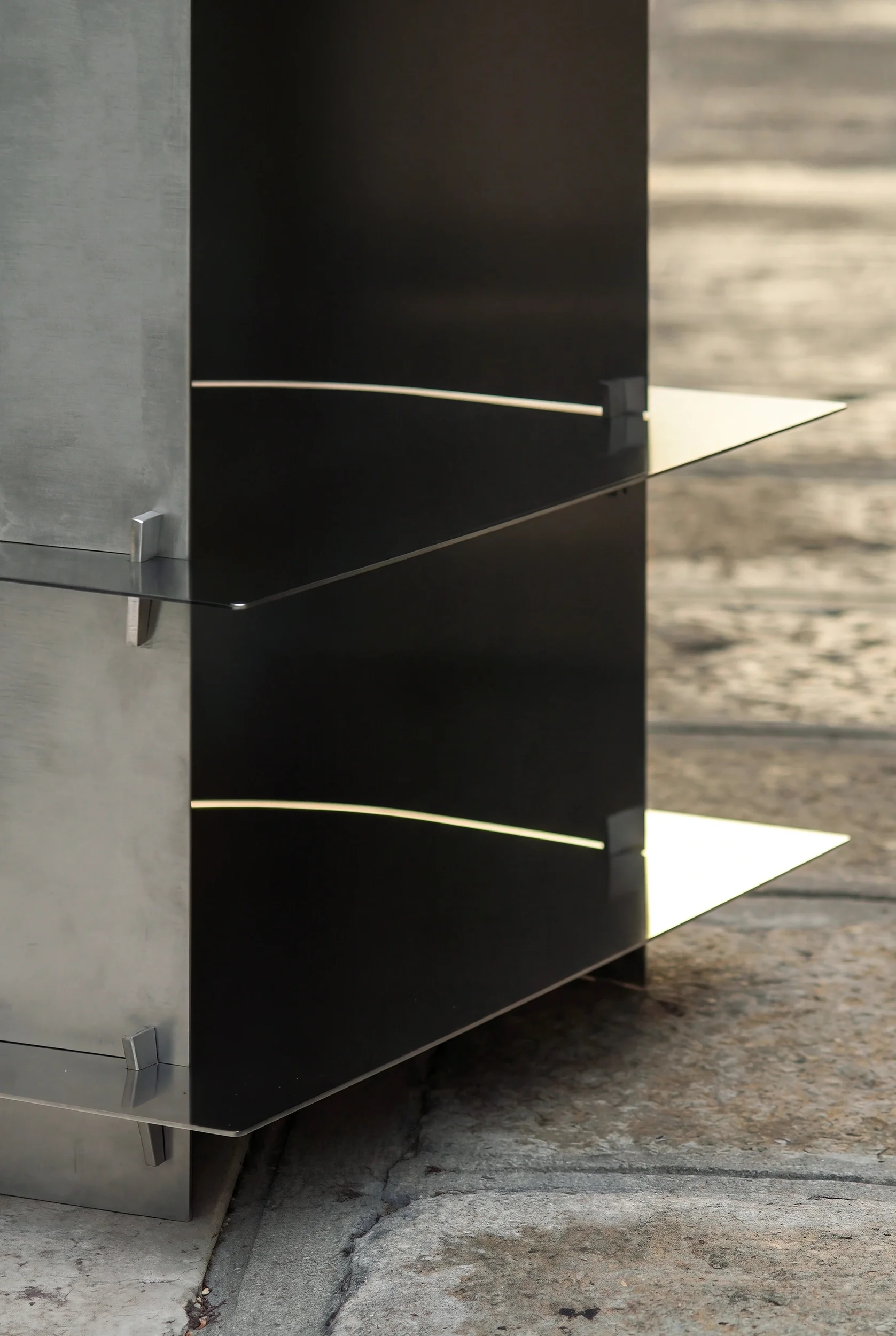 Angolo di una cucina moderna con ante nere lucide e ripiani in acciaio, su pavimento di pietra.