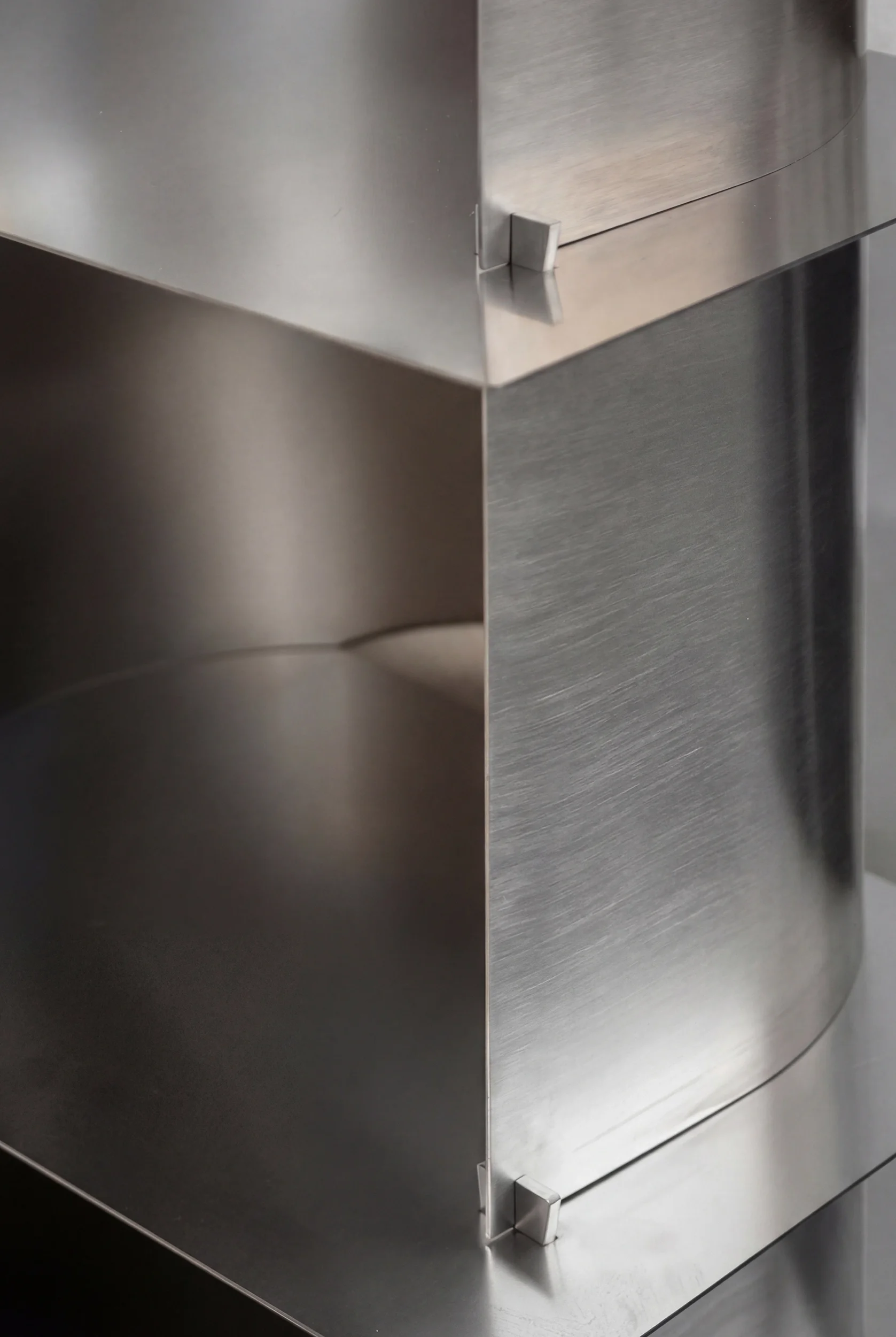 Due armadietti di metallo in acciaio inossidabile con superfici lisce e lucide, uno visibile di lato e uno di fronte, con angoli arrotondati.