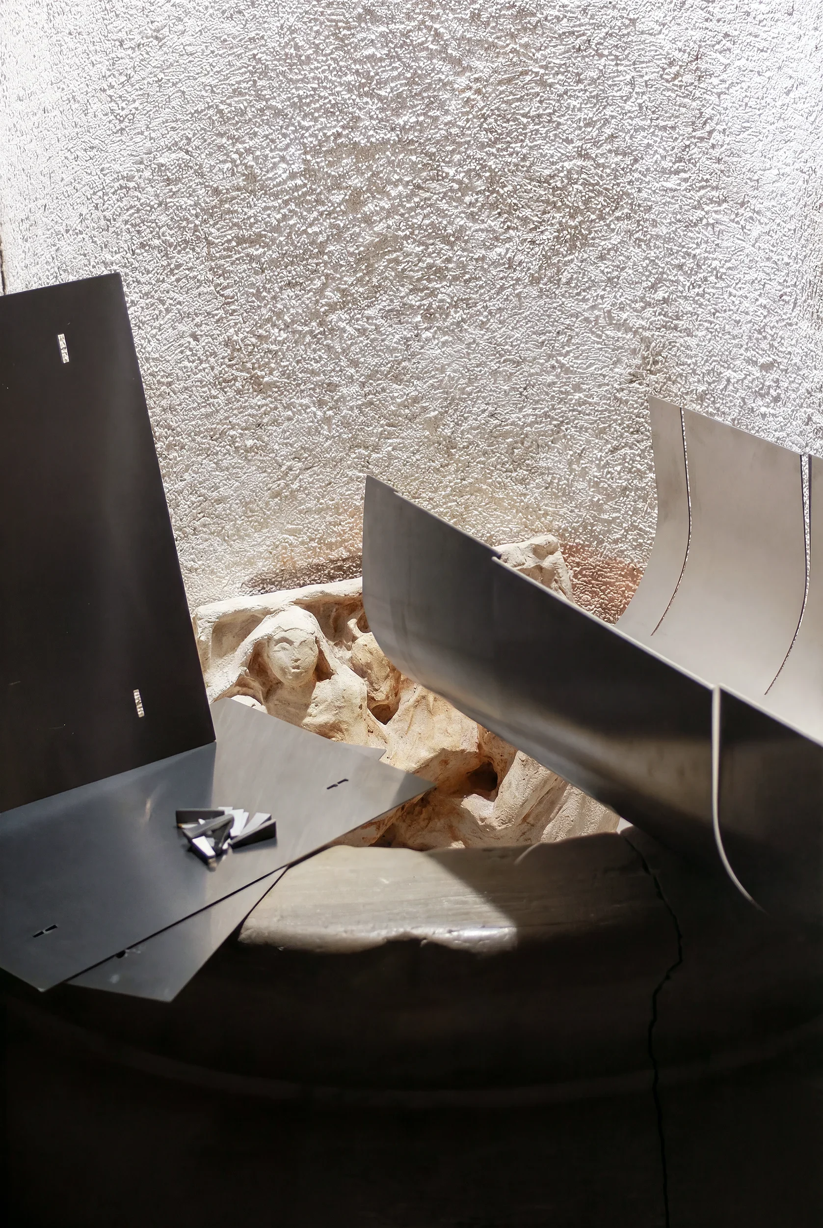 Ingresso di un edificio con pareti di cemento grezzo e arredi di design in metallo, con pietre e rocce visibili nella zona.