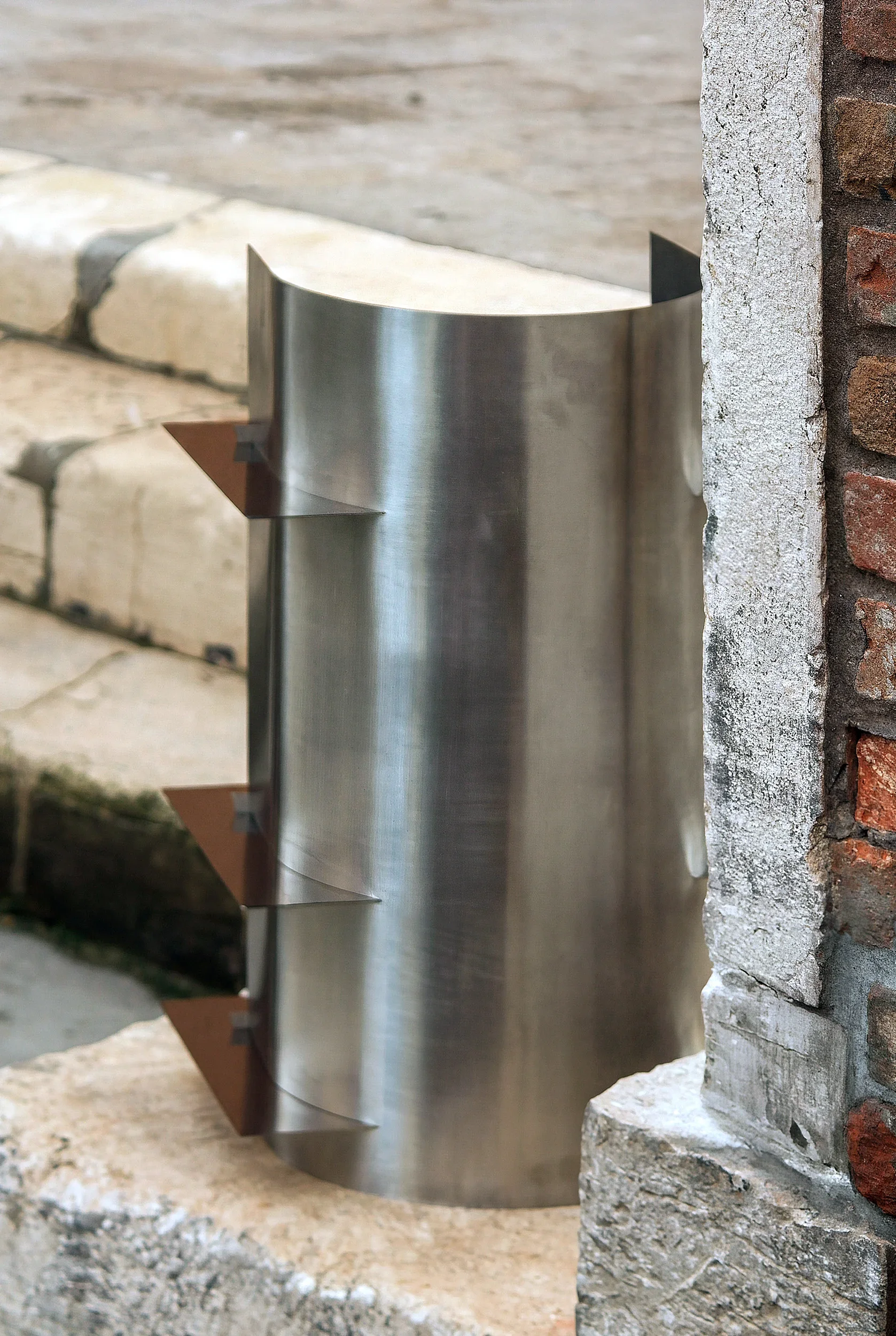 Una cappa di aspirazione in metallo con quattro alette di supporto, montata tra un muro di mattoni e un bordo di pietra.