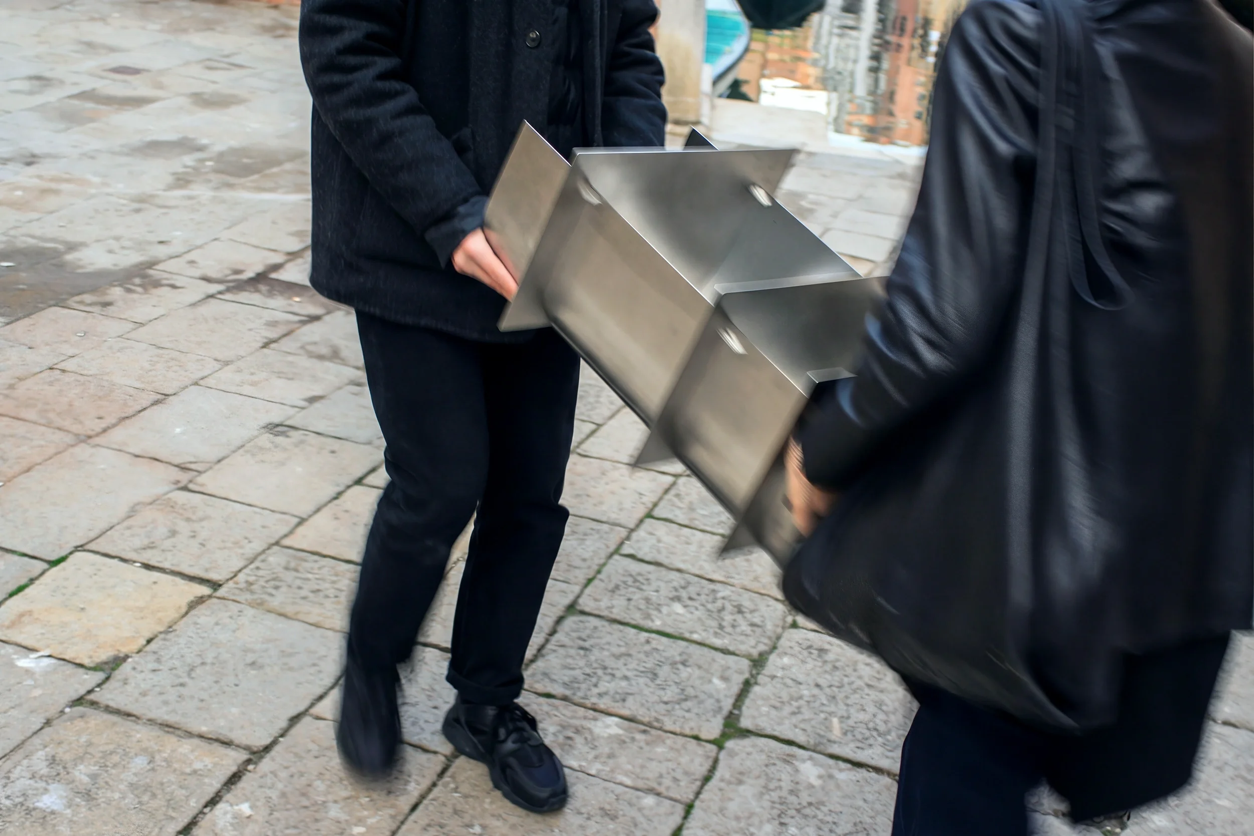 Due persone stanno scambiando un contenitore di metallo, probabilmente per l'acqua, su una strada di ciottoli.