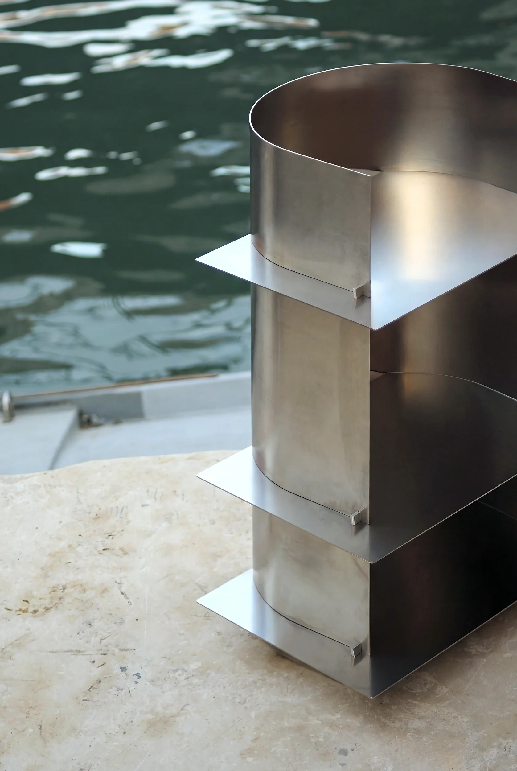 struttura in acciaio inossidabile con forme curve, posizionata sulla spalla di una pietra, vicino all'acqua