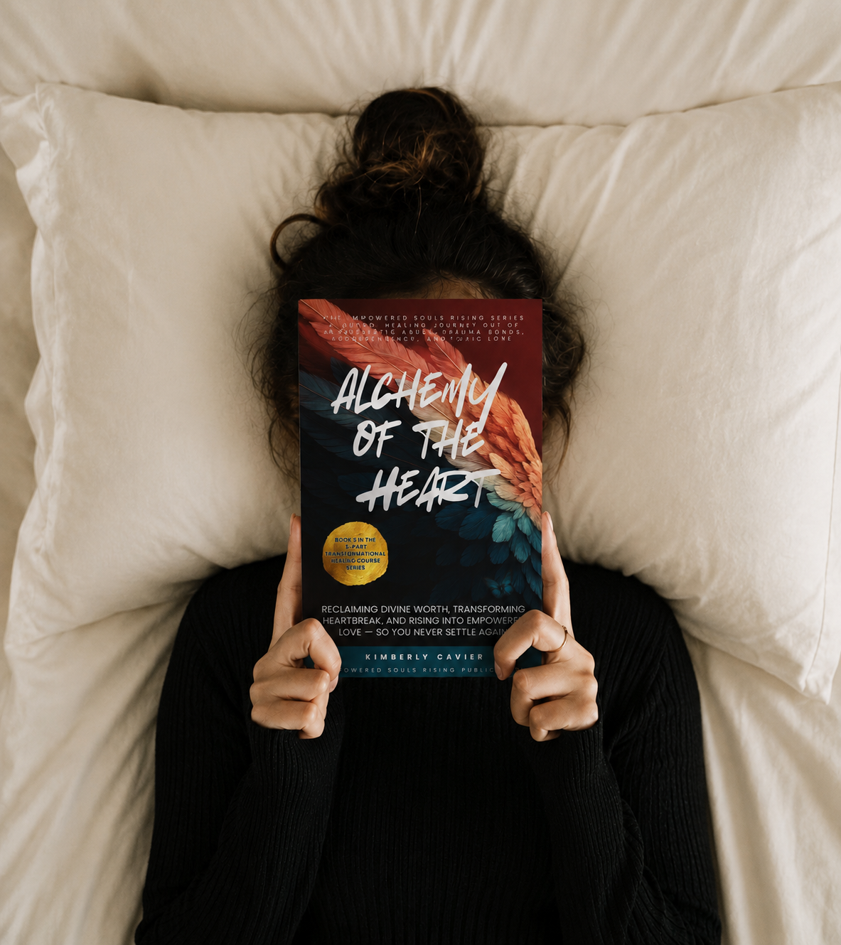 Person resting in bed holding Alchemy of the Heart by Kimberly Cavier, a healing workbook for heartbreak, self-worth, and healthy love after toxic relationships.