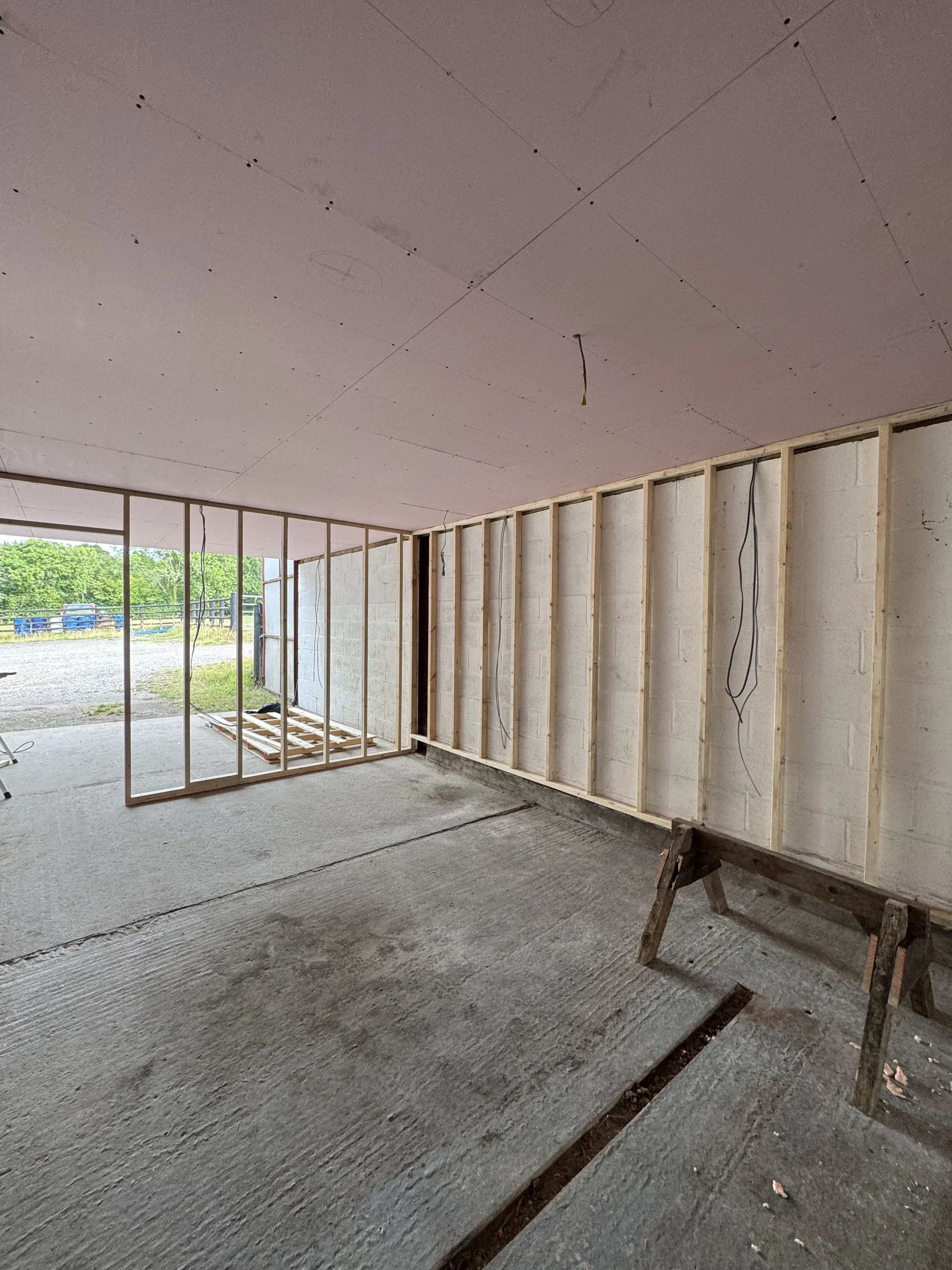 Interior of a building under construction with exposed wooden framing and drywall installation on the ceiling.