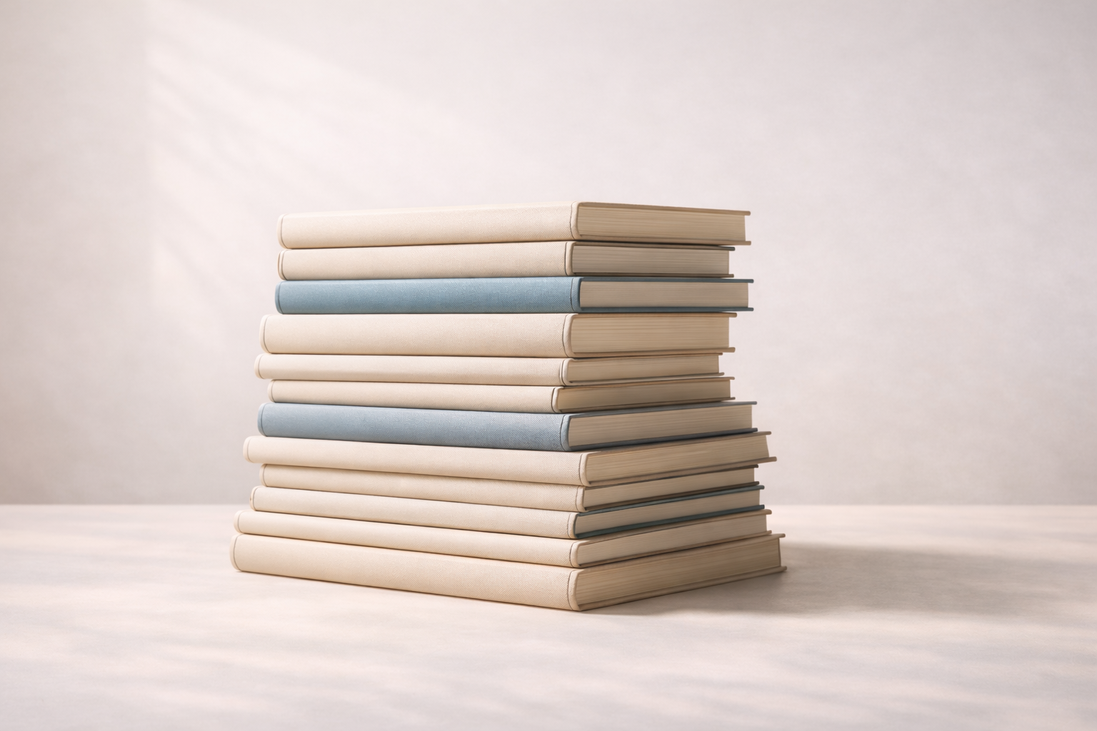 A stack of hardcover books with pastel-colored covers on a light surface against a neutral background.