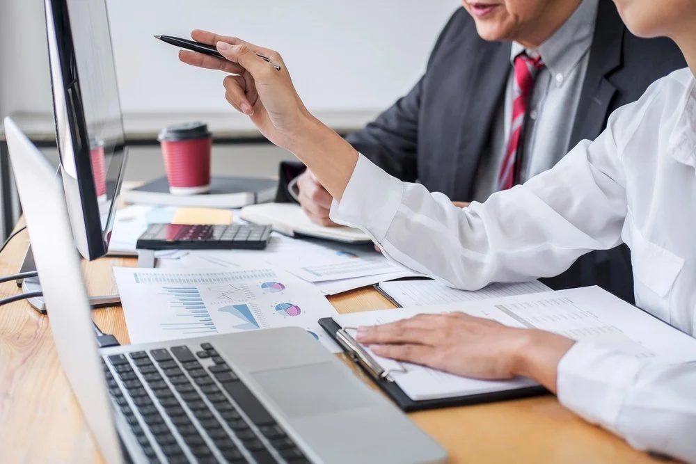 Two individuals sitting at a table overlooking charts with their computers and building out a financial model.