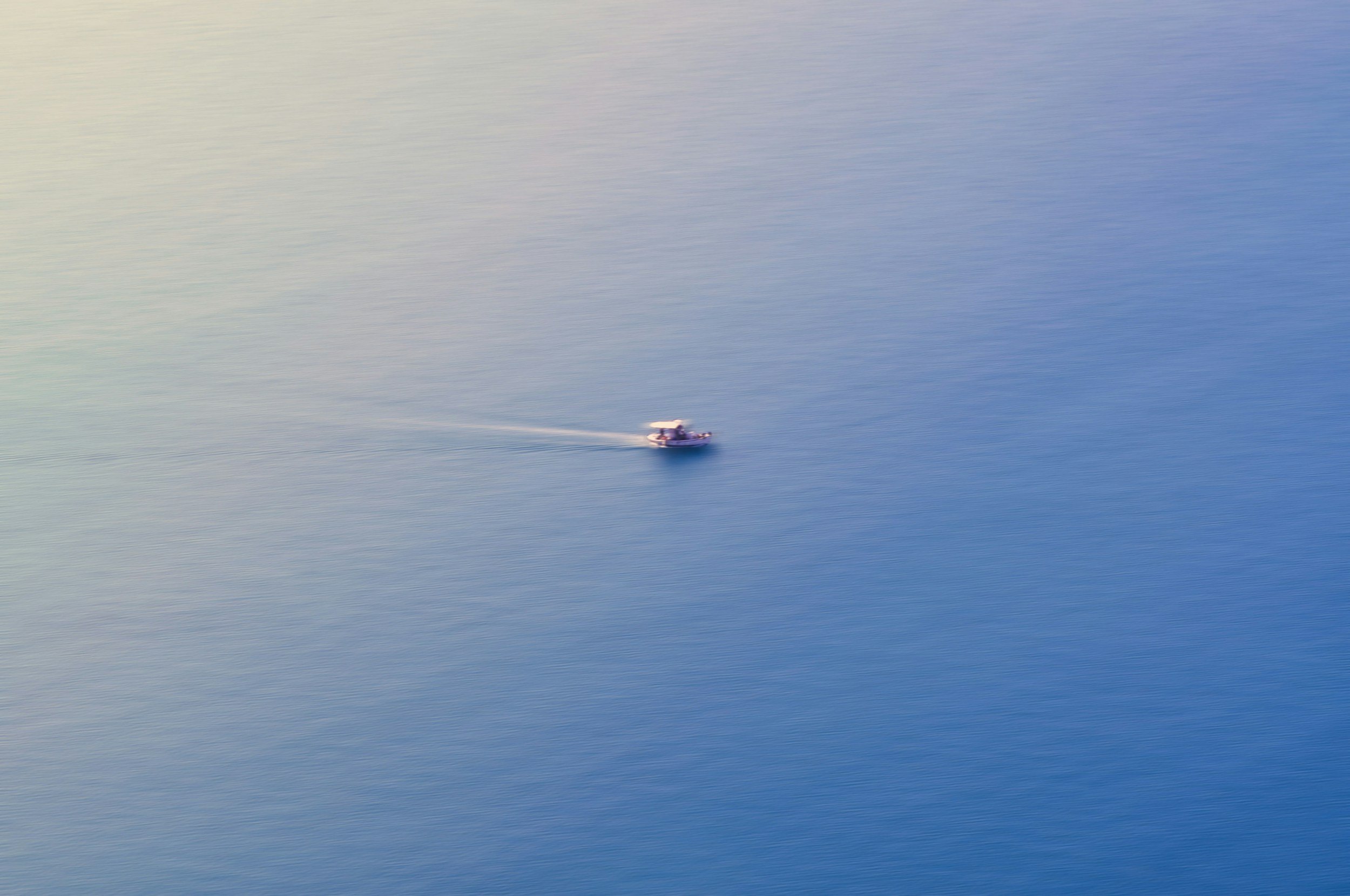 Een klein wit bootje die door kalm water vaart, met een witte en blauwe kleurige achtergrond
