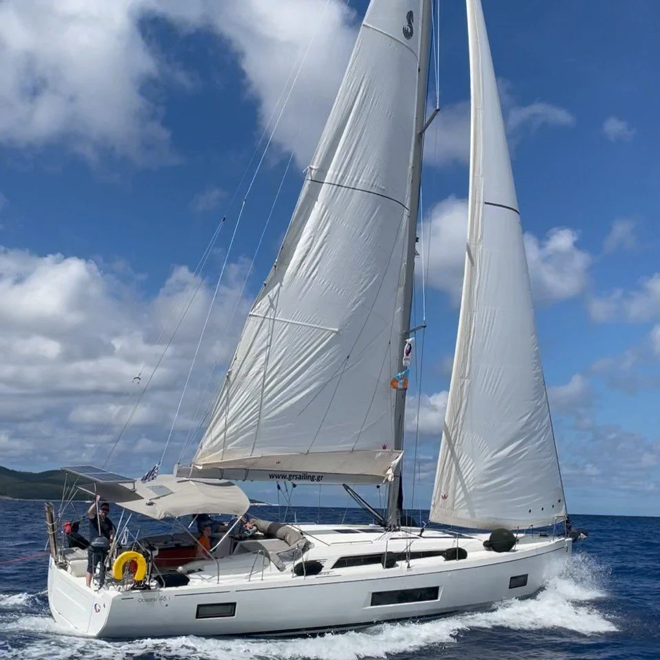 Sailboat met witte zeilen op de blauwe zee onder een bewolkte hemel.