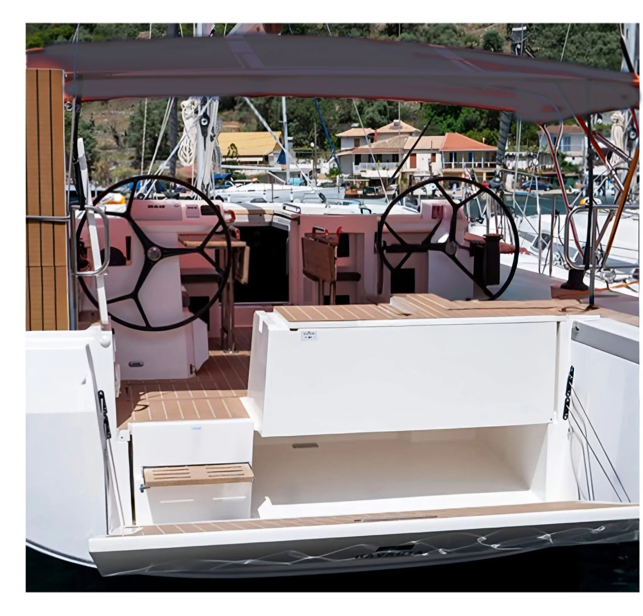 Binnenzicht van een jacht met een shelter en teak hout op de vloer, met een uitzicht op huizen en boten in de haven op de achtergrond.