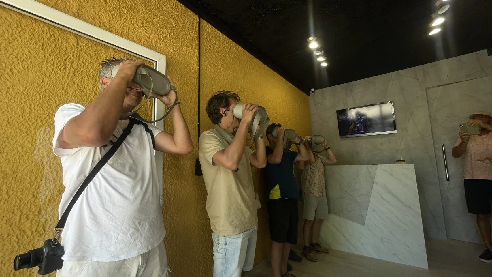 Vijf mensen kijken door virtuele realiteit brillen in een moderne kamer met gele en marmeren muren.
