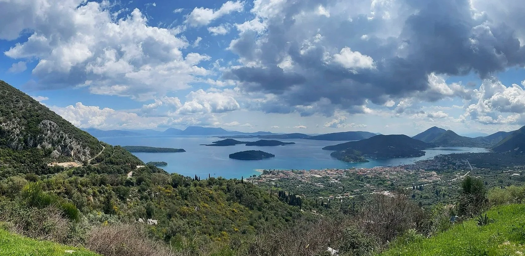 Uitzicht over een meer met eilanden, omgeven door bergen onder een deels bewolkte hemel.