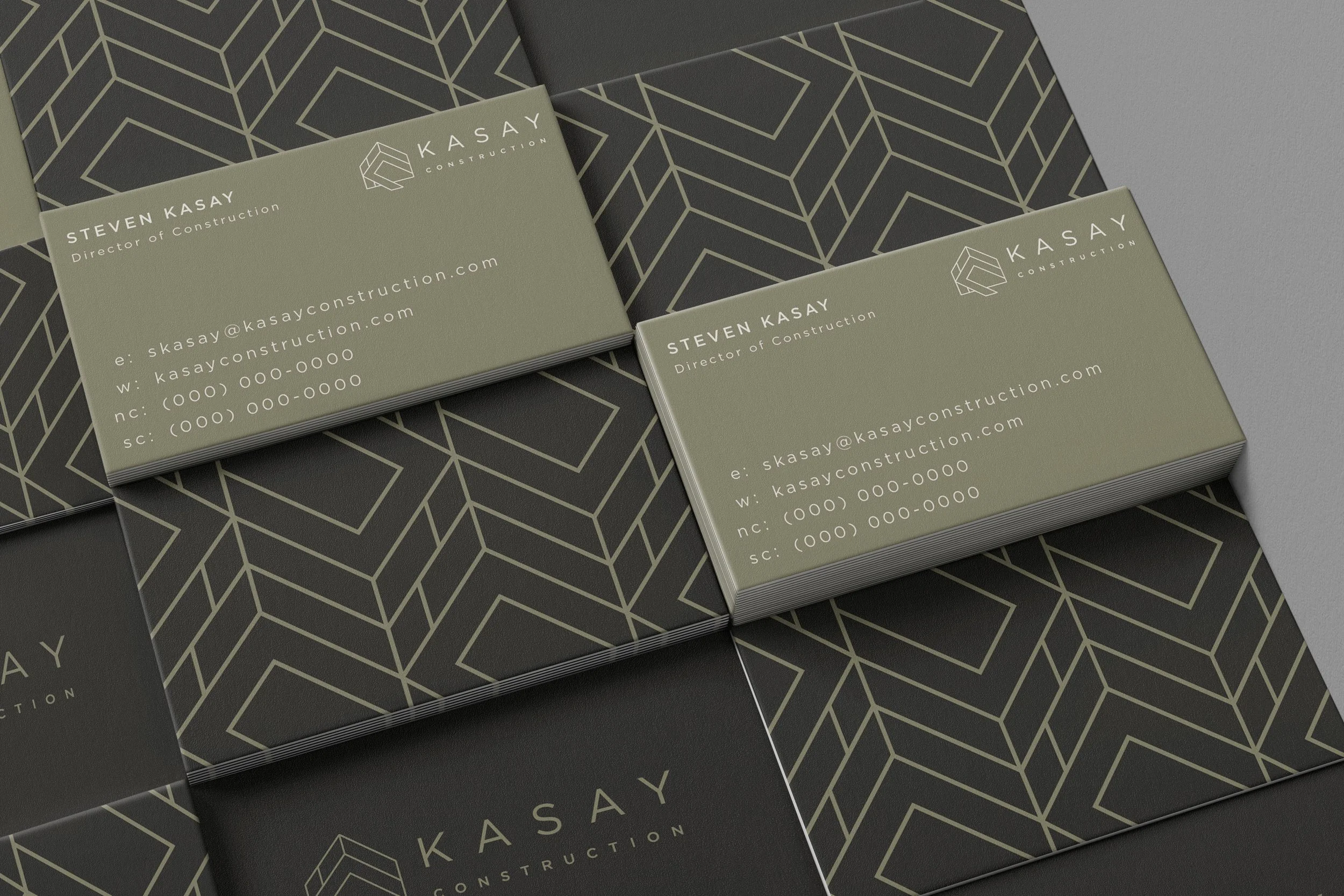 Business cards for Kasay Construction with a geometric logo and contact details, placed on a patterned surface.