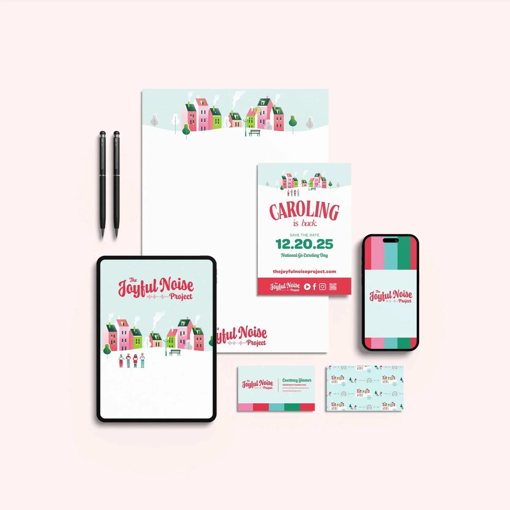 Collection of promotional materials and digital devices for The Joyful Noise Project, featuring colorful illustrations of houses, event details for Caroling on December 20, 2025, and branded merchandise including business cards, flyers, a phone, and an iPad.