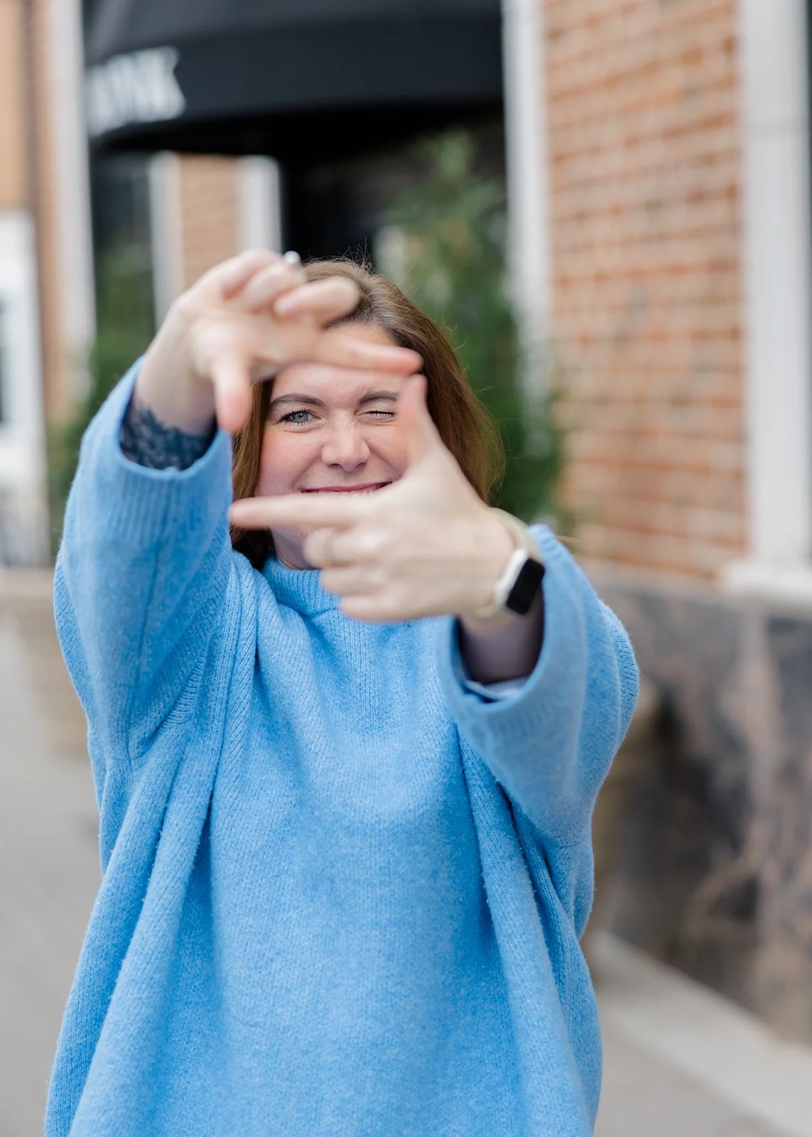Woman with a smartwatch making a frame with her hands and smiling outdoors.