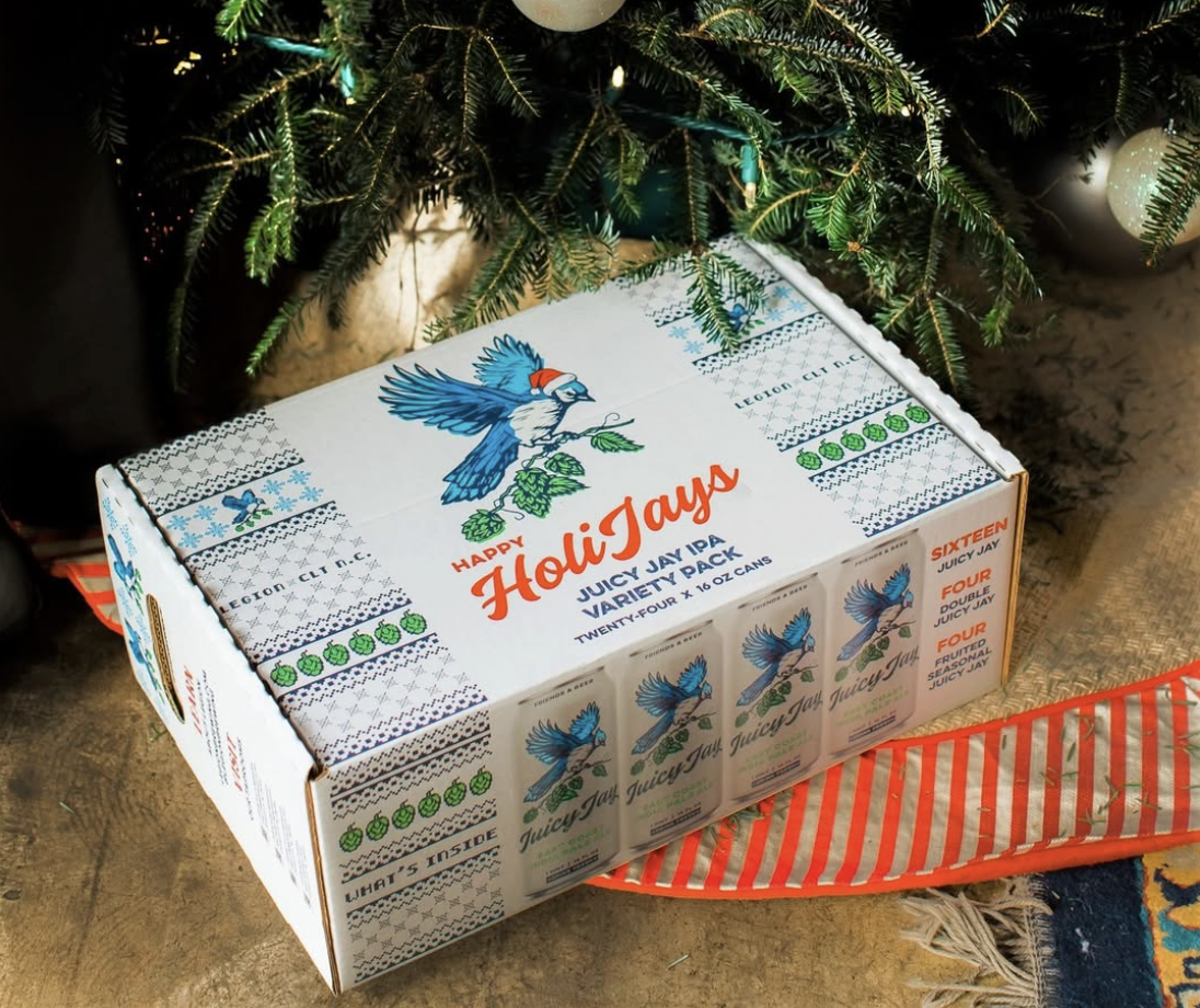 A box of Juicy Jay's variety pack of hemp wraps under a decorated Christmas tree with wrapped gifts nearby.