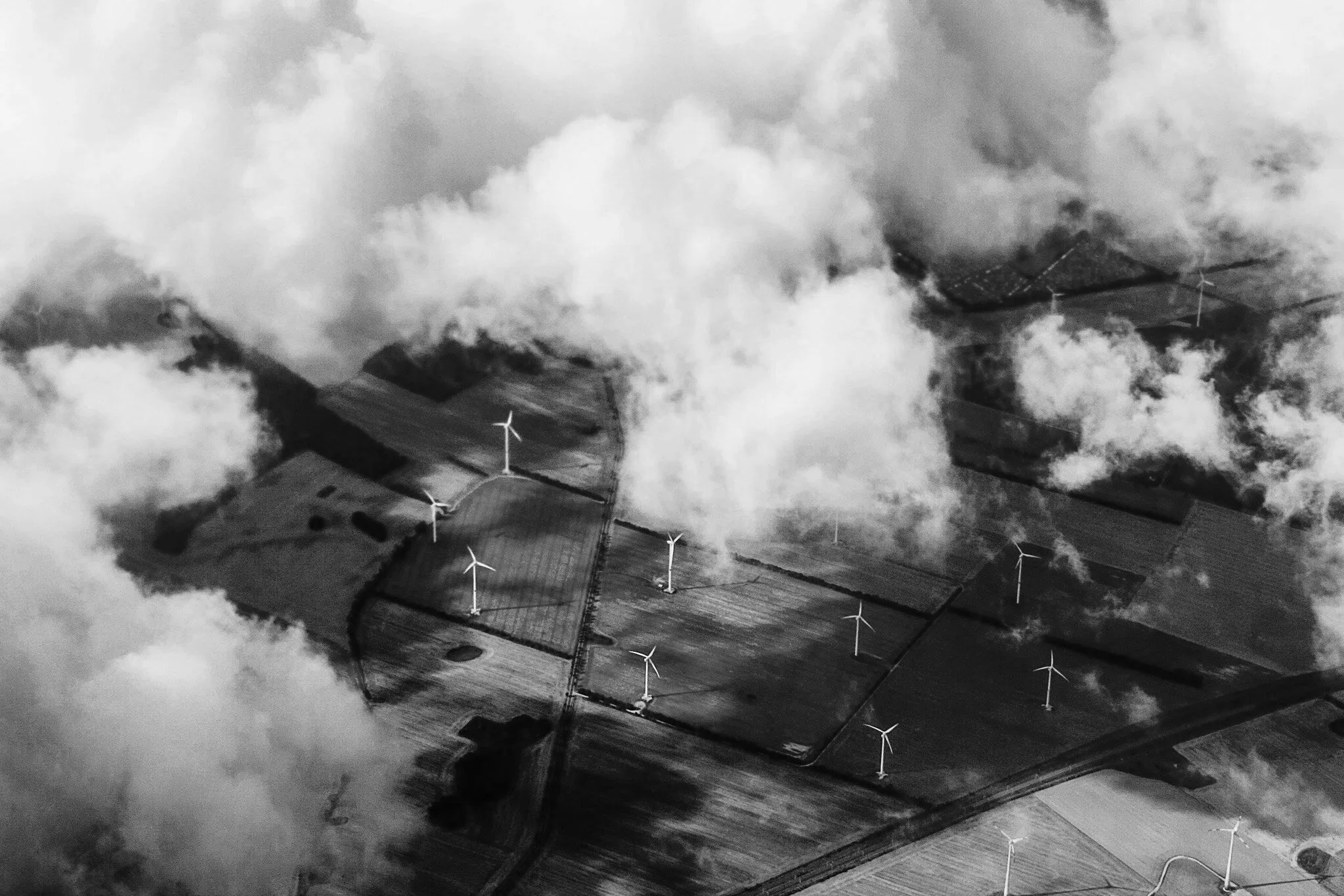 Aerial view of farmland with wind turbines, partially obscured by clouds and fog.