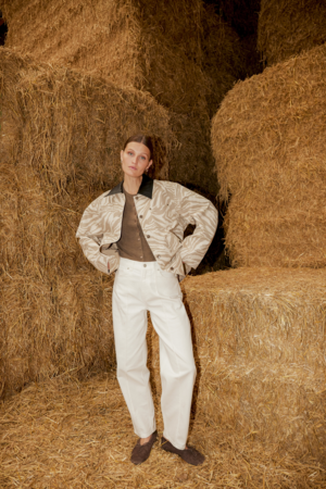 A woman standing inside a barn with large hay bales surrounding her.