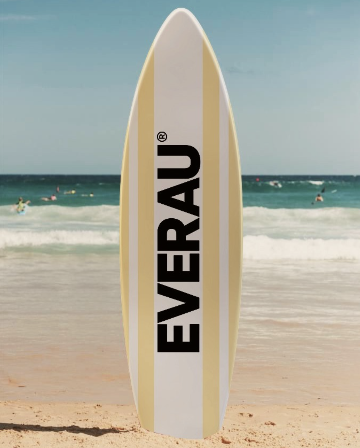 A surfboard with the brand name 'EVERAUV' written in black on a white panel, standing upright on a sandy beach with the ocean and people in the water in the background.
