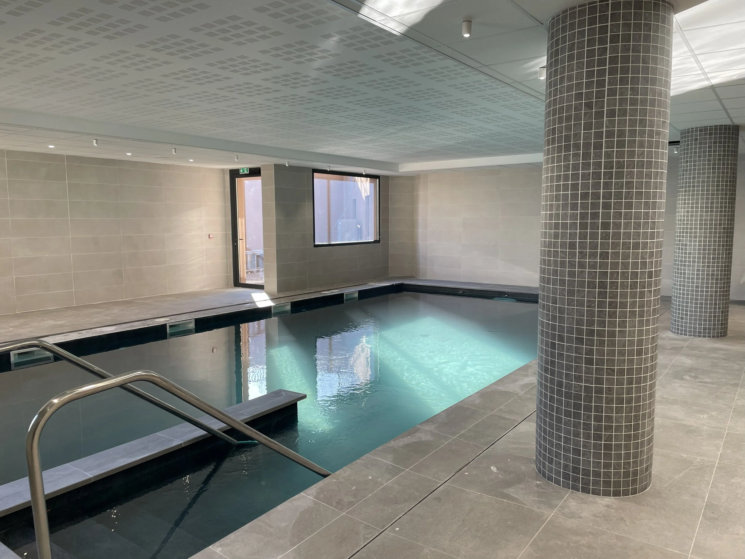 Piscine intérieure avec sol carrelé antidérapant et poteau habillé de mosaïque, revêtements adaptés aux zones humides d’un espace bien-être