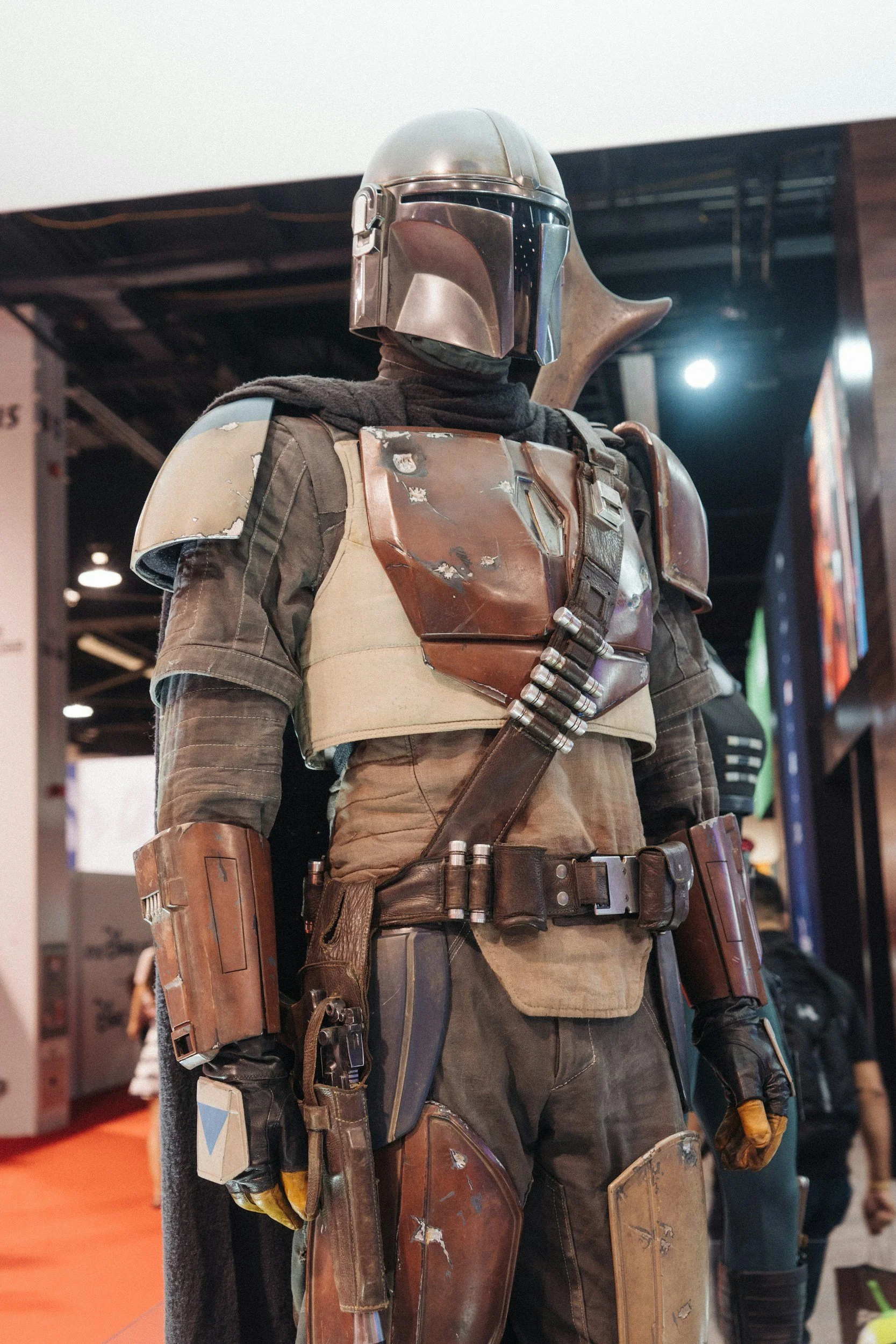 A life-sized cosplay of the character Boba Fett from Star Wars, detailed with armor, helmet, and weapons, displayed at a convention.