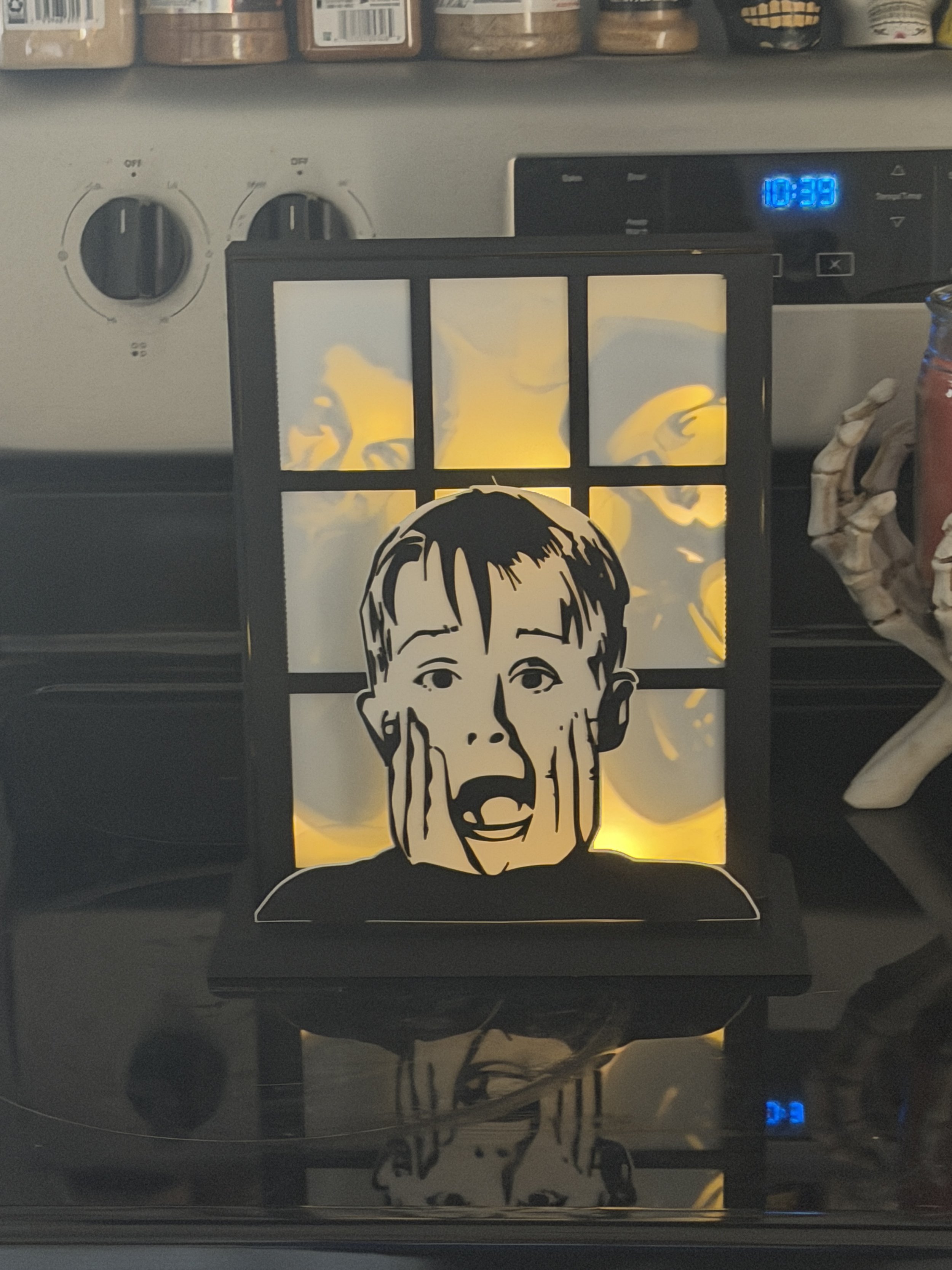 A decorative light with a cartoon drawing of a surprised boy with hands on his face, placed in front of a kitchen stove.