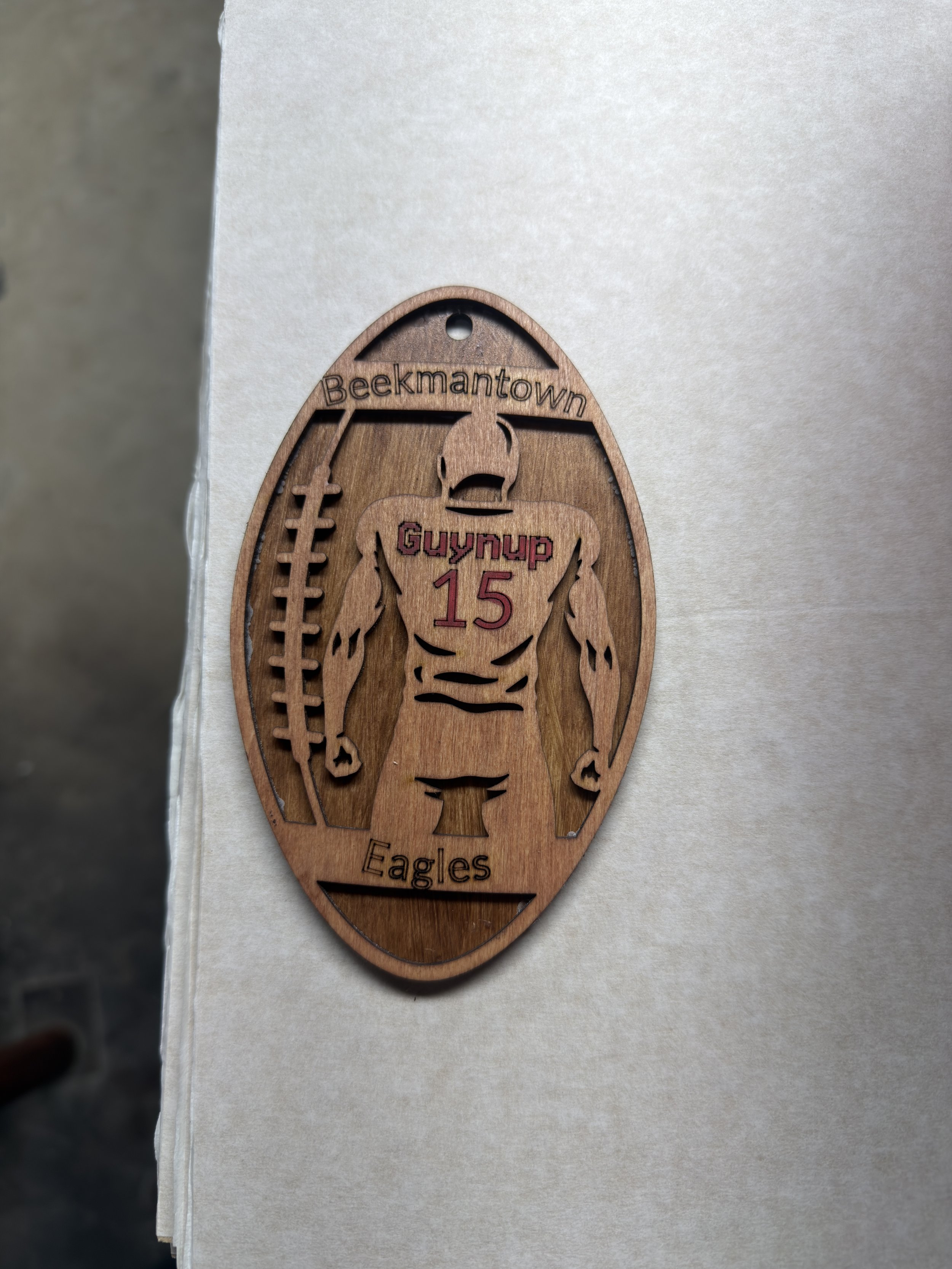 Wooden emblem with a muscular football player silhouette, surrounded by text 'Beekmantown Eagles,' with 'Guynup 15' on the chest and a football on the side.