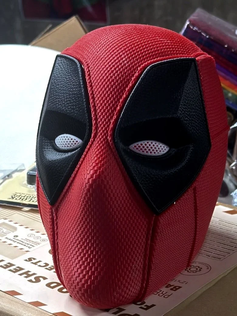 A red backpack designed to look like Deadpool's face, featuring black eye patches and mesh details.