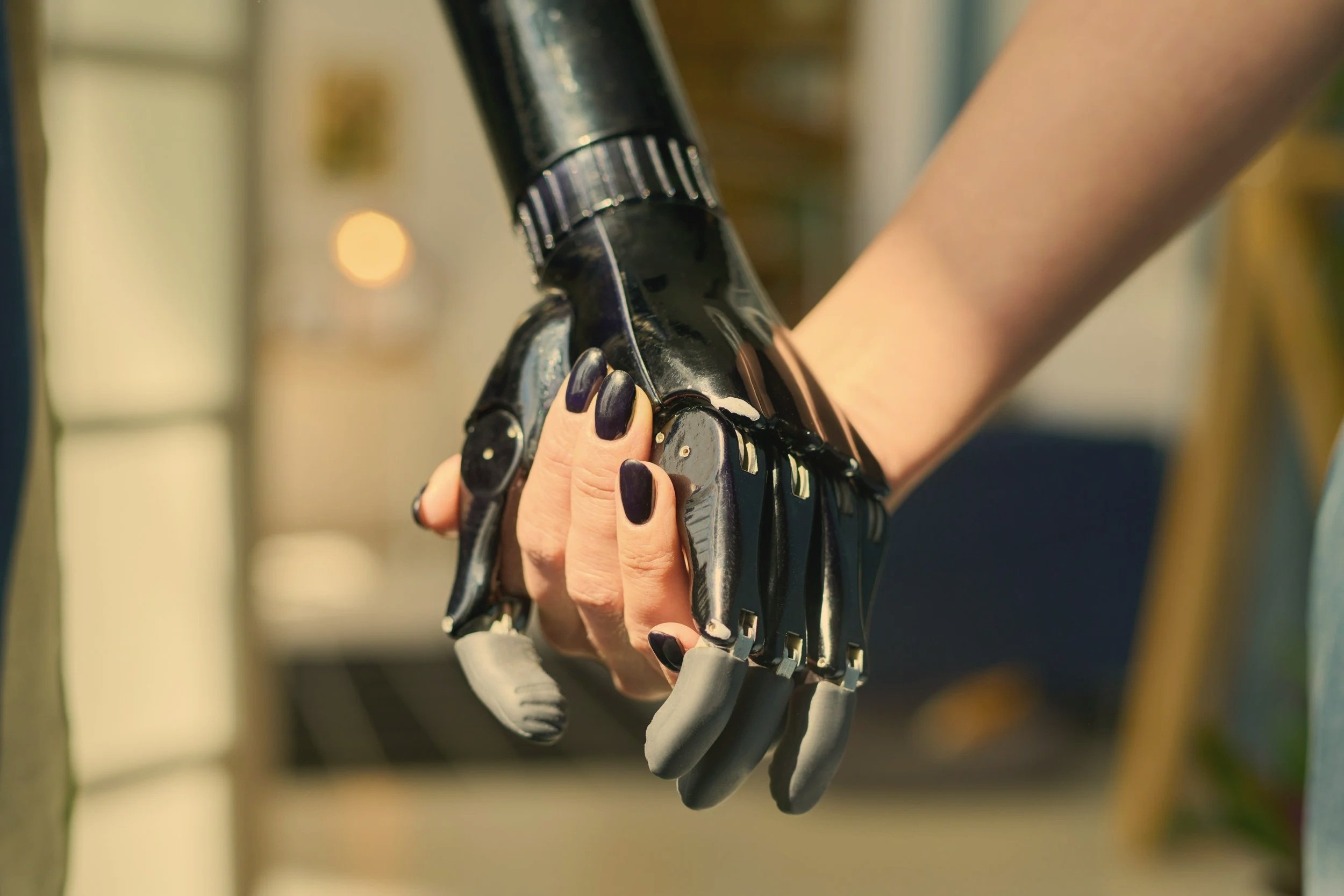Close-up of a human hand holding a robotic hand with metallic fingers and joints.