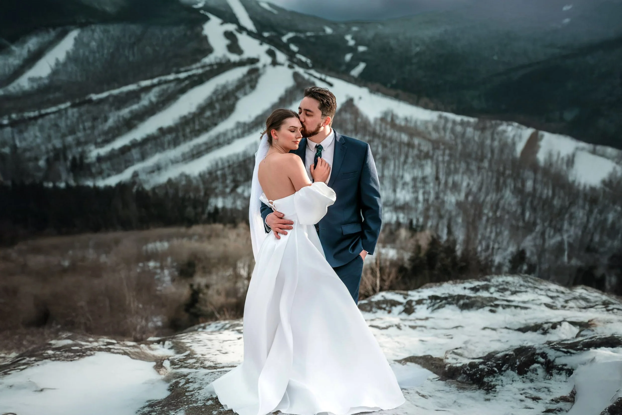 A bride and groom embrace outdoors on a snowy mountain landscape.