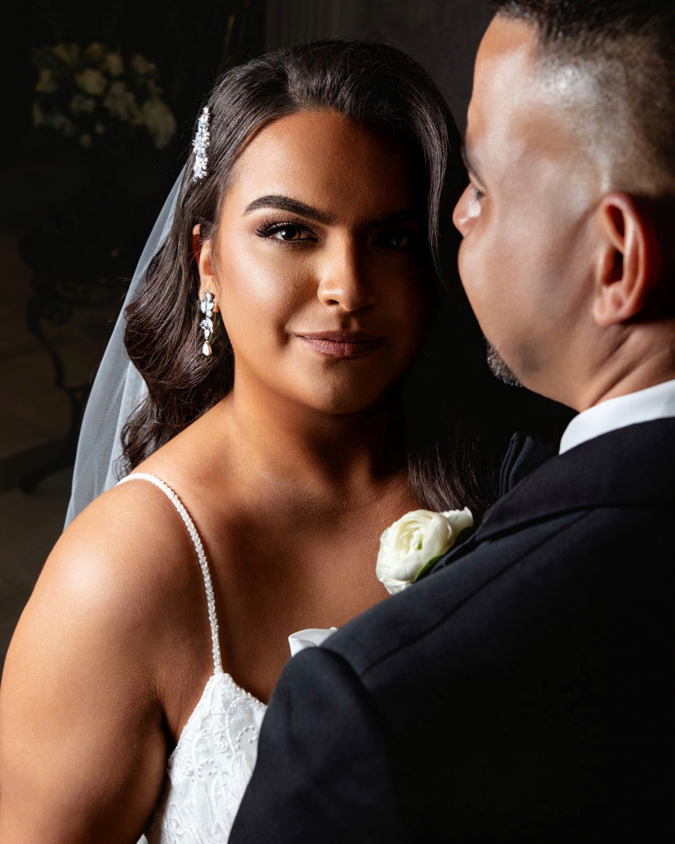 Bride and groom at their wedding, close-up portrait with joyful expressions, bride wearing white wedding dress and veil, groom in black tuxedo, bride holding a white rose