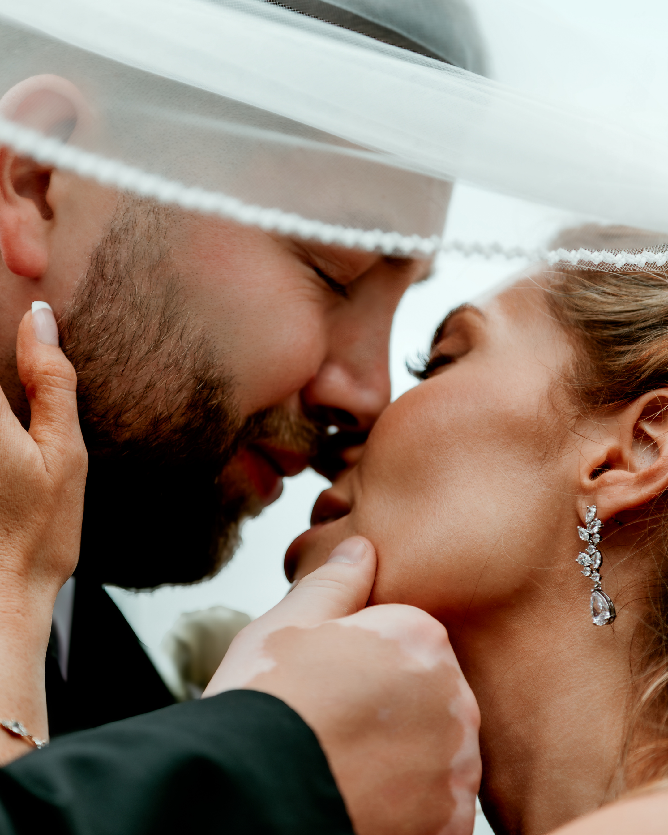A close-up of a couple touching foreheads and noses, about to kiss, with the woman wearing sparkling drop earrings, and the man wearing a cloth hat.