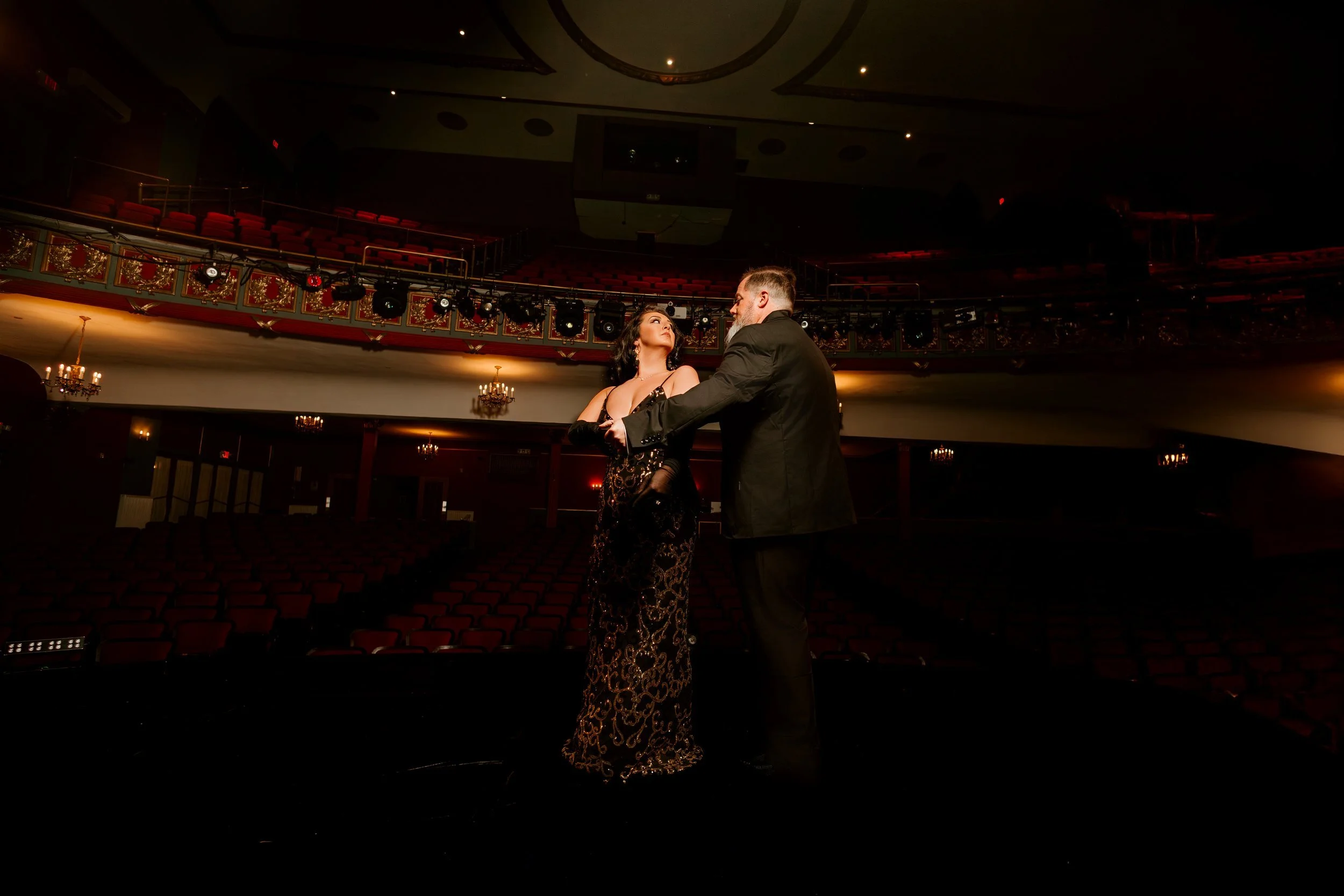 A couple dancing on stage in a theater with red seats and ornate decorations.
