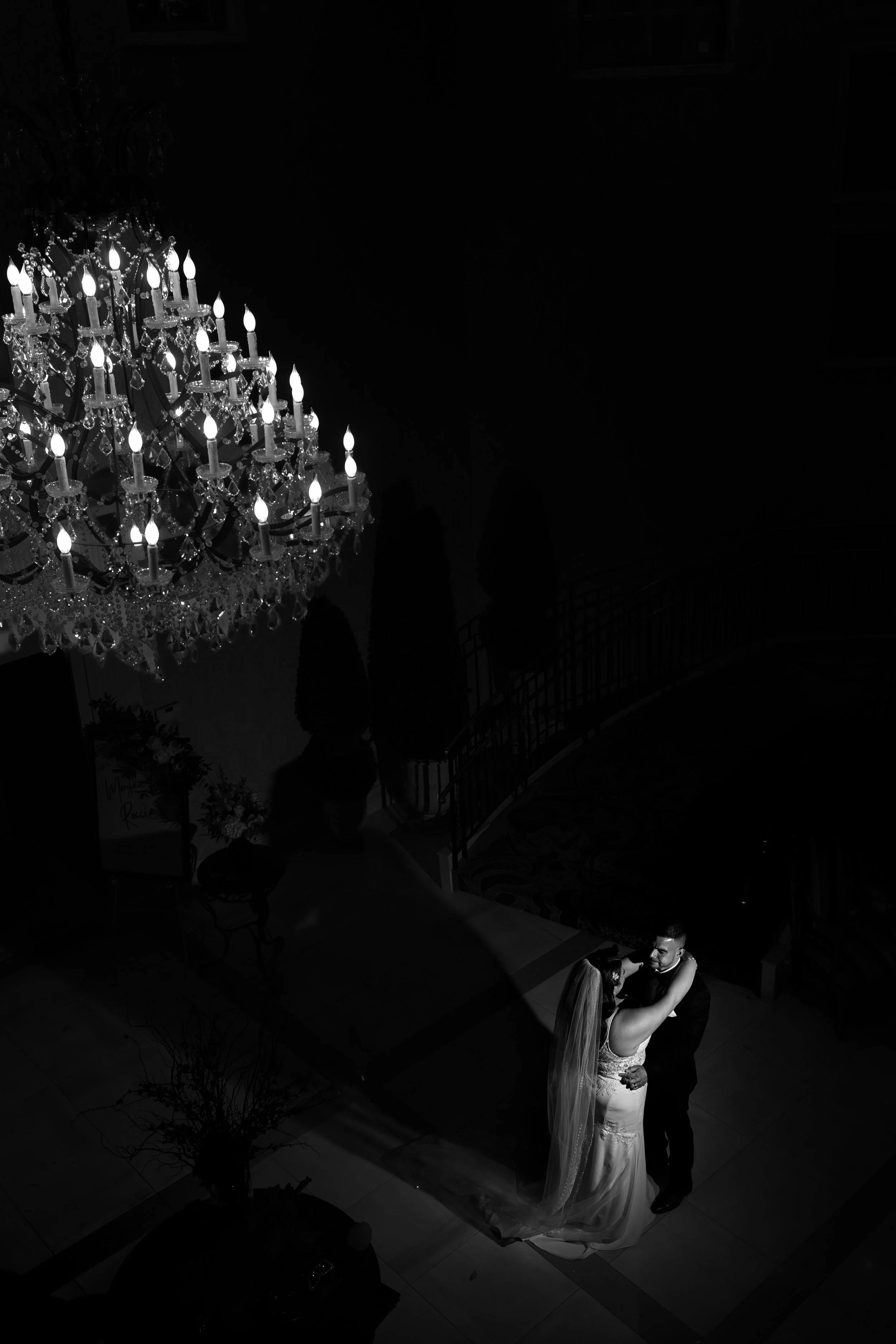A bride and groom dancing beneath a chandelier in a dark room during their wedding.