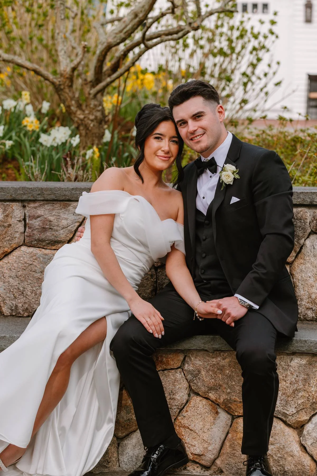 Romantic wedding portrait of a bride and groom at Wequassett Resort in Harwich, MA, featuring an off-the-shoulder white gown, black tuxedo, and spring florals at a luxury Cape Cod wedding venue.