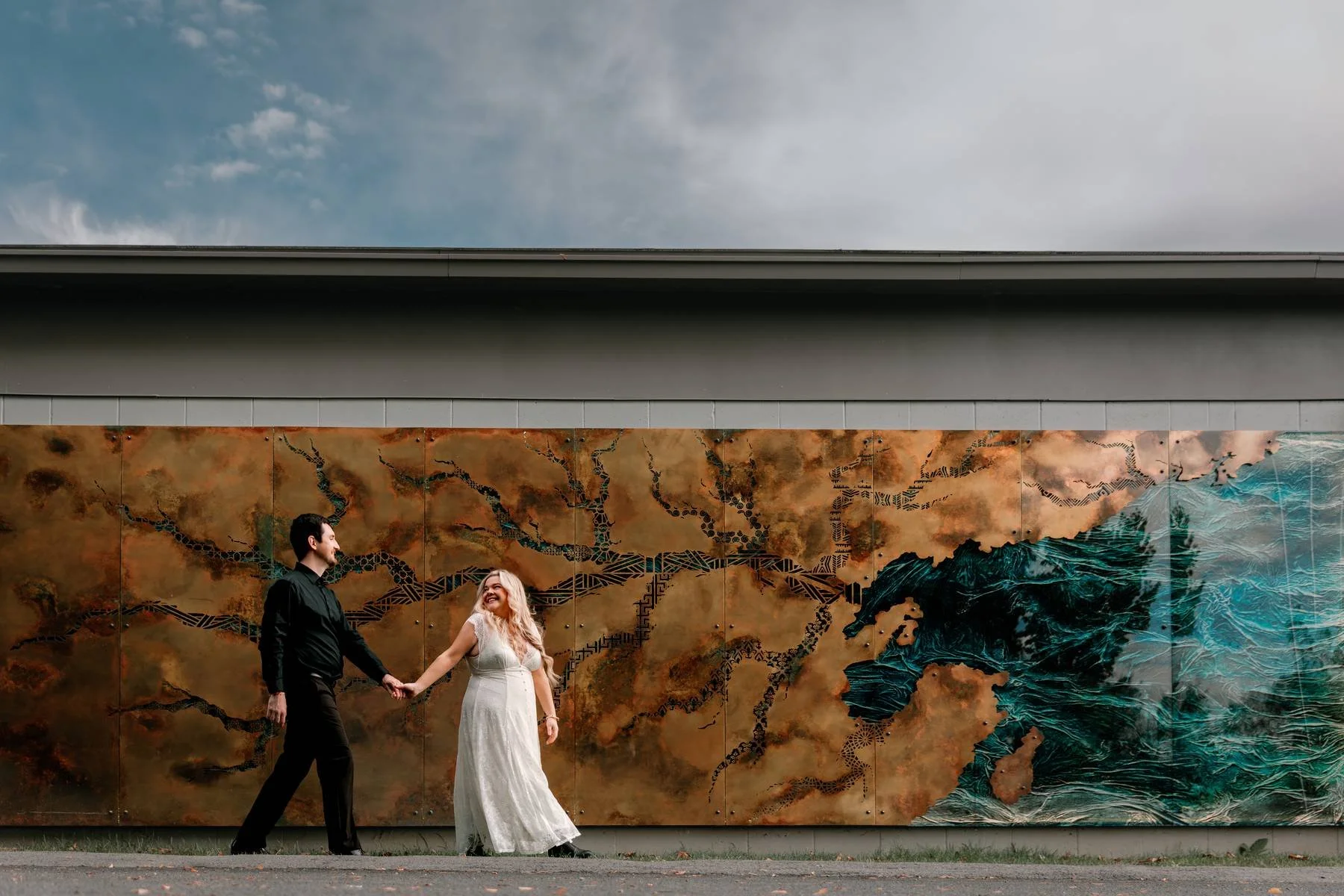 A couple holding hands and walking in front of a wall mural depicting a map with mountains and water.