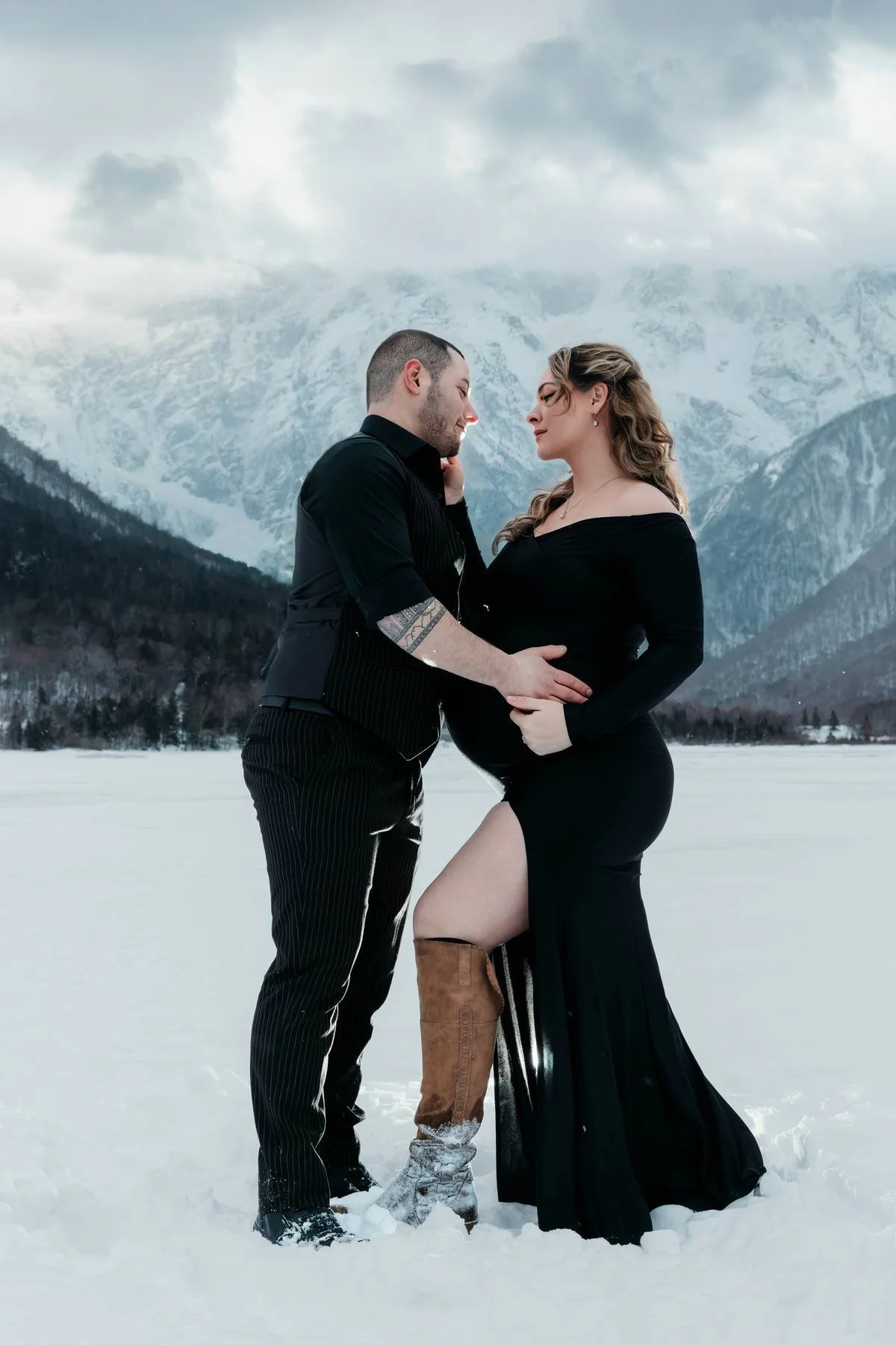 A man and woman in black clothing standing closely together in a snowy landscape with snow-capped mountains in the background.