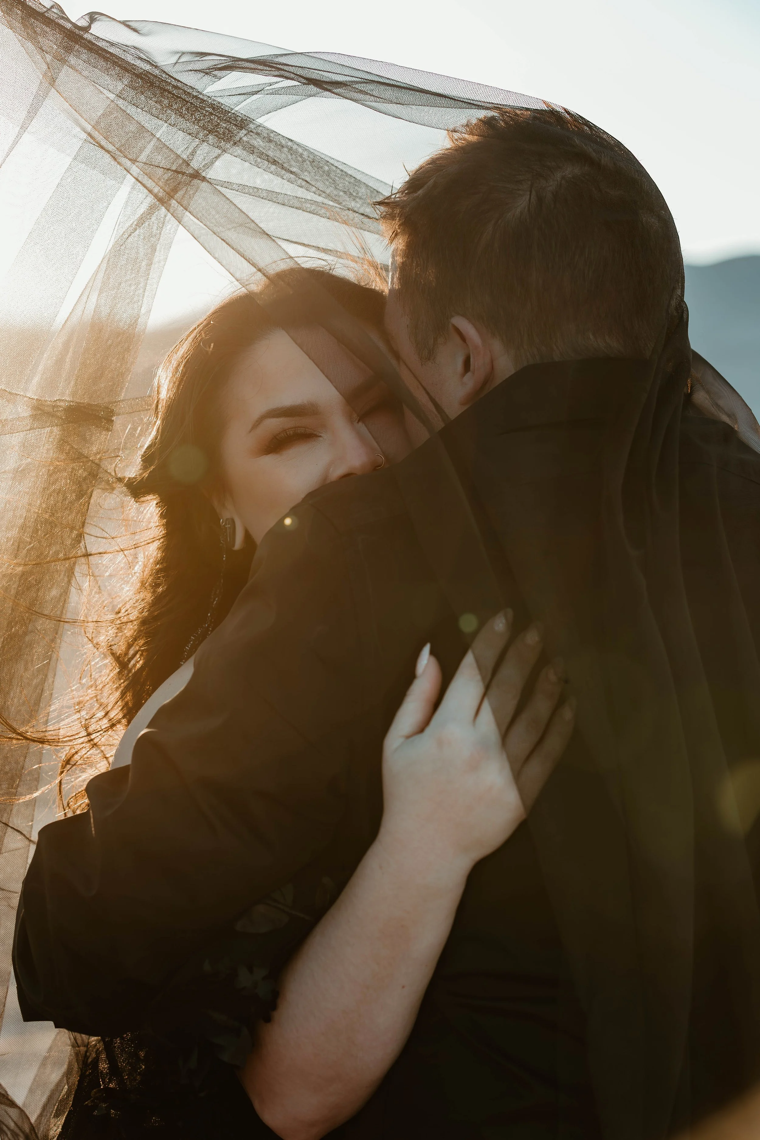 A couple embracing outdoors with sunlight shining through a sheer fabric, capturing an intimate moment.