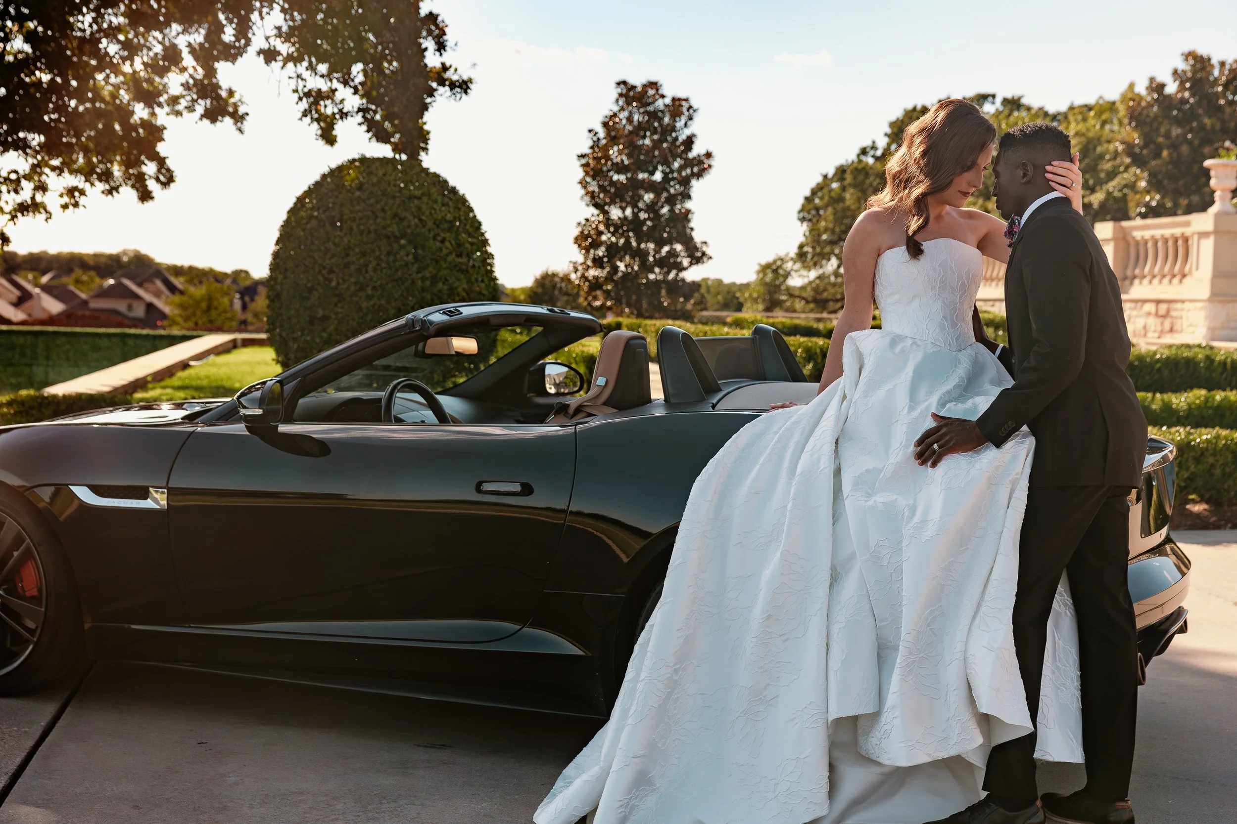 A bride and groom share a romantic moment beside a black convertible car on their wedding day.