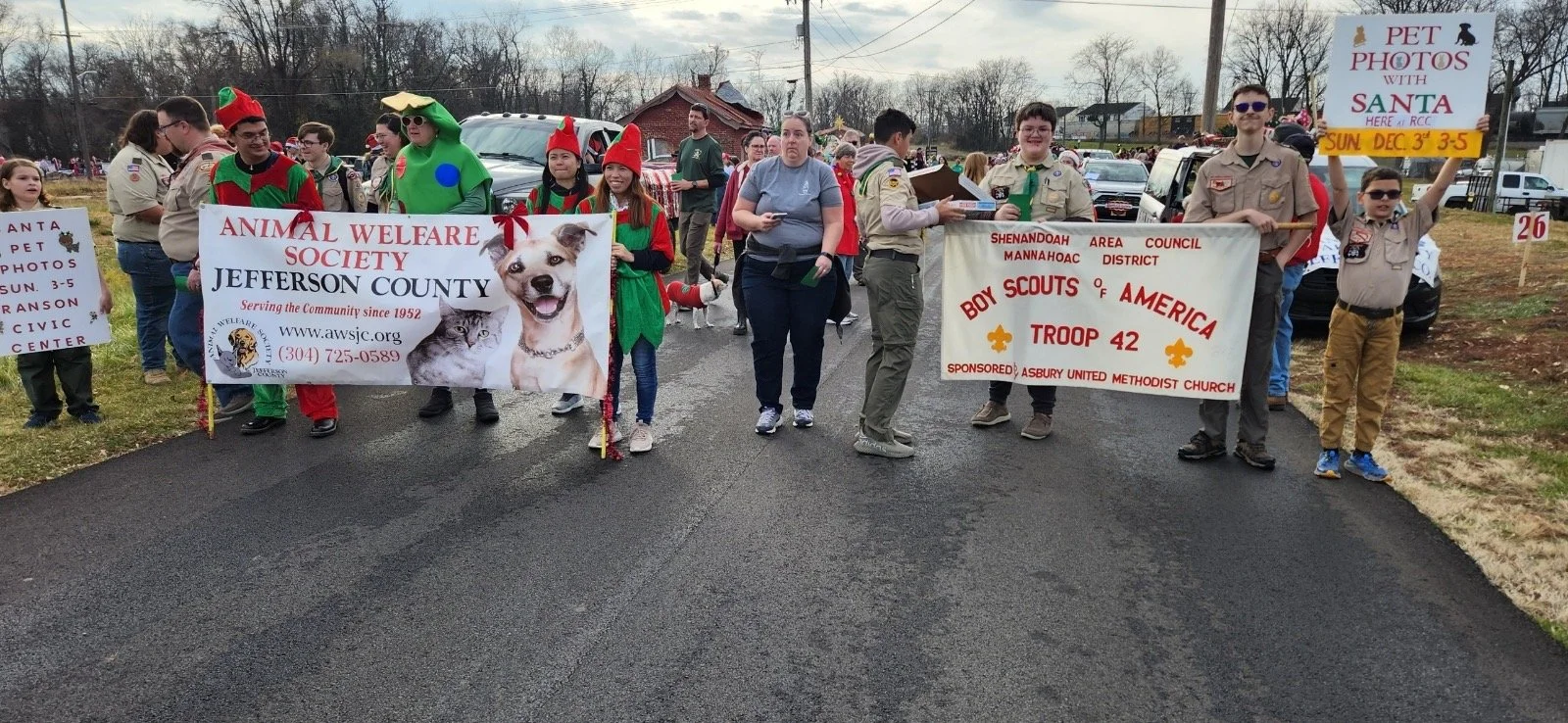 Group of Boy Scouts and community members participating in a parade or walk, holding banners promoting animal welfare and community support, with some people dressed in festive costumes.